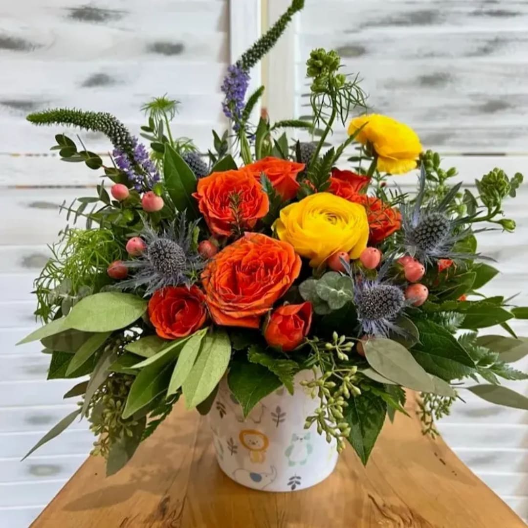 Colorful bouquet of orange and yellow roses in a patterned container