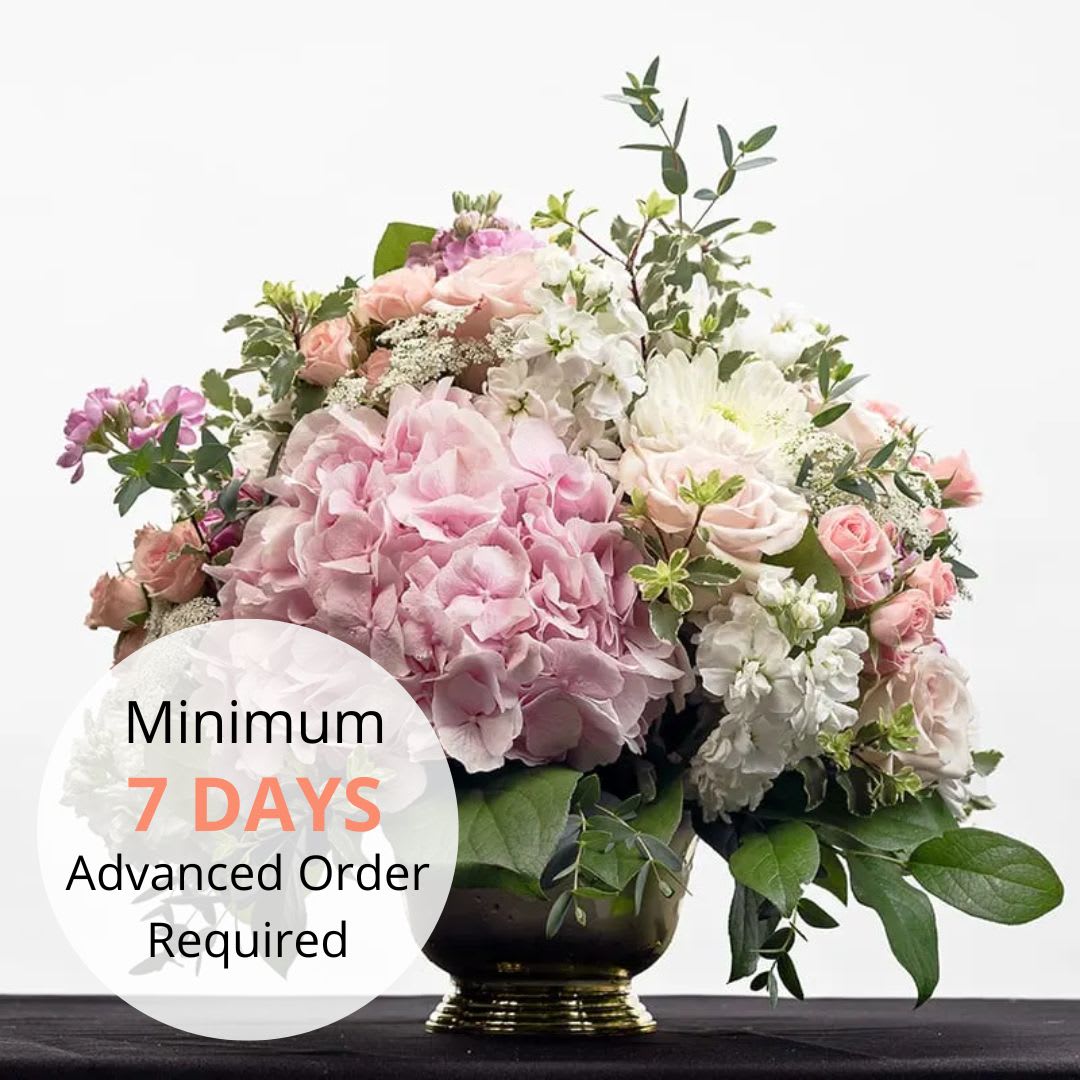 Pastel pink and white hydrangea and rose arrangement in a gold pedestal vase