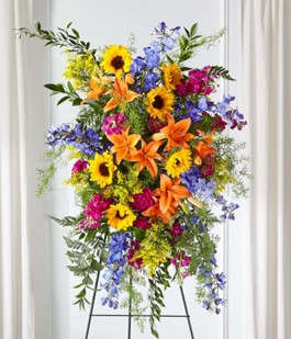 Tall standing floral spray with sunflowers, lilies, and blue flowers