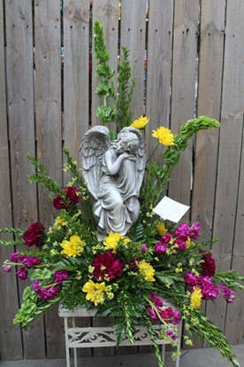 Floral arrangement with an angel statue and bright yellow, magenta, and red flowers