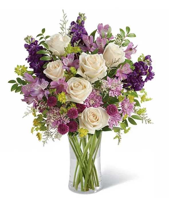 Bouquet of white roses and purple flowers in a clear glass vase