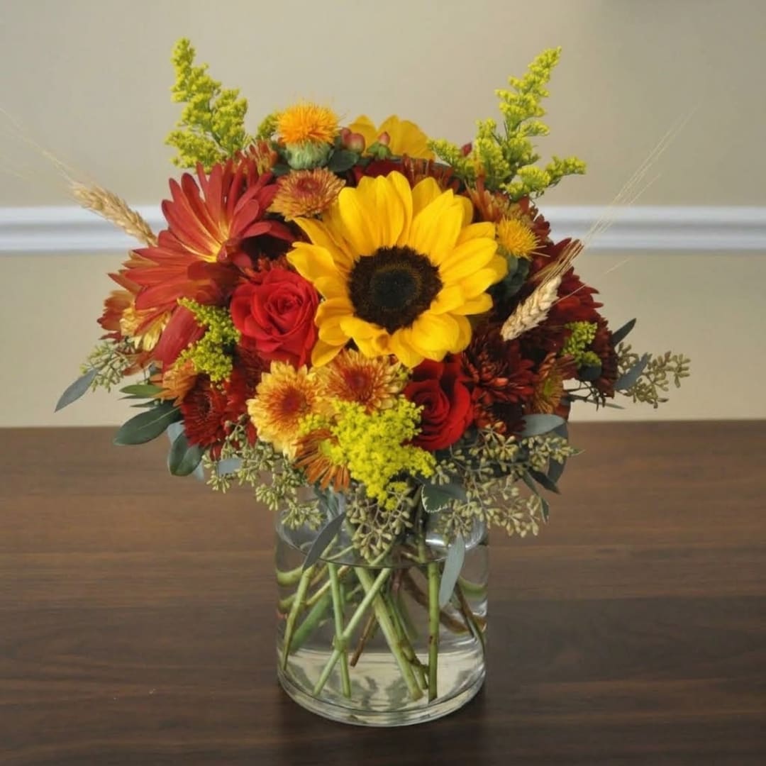 Mixed bouquet of sunflowers, red roses, and autumn flowers in a glass vase