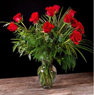 Red roses arranged in a clear glass vase with greenery