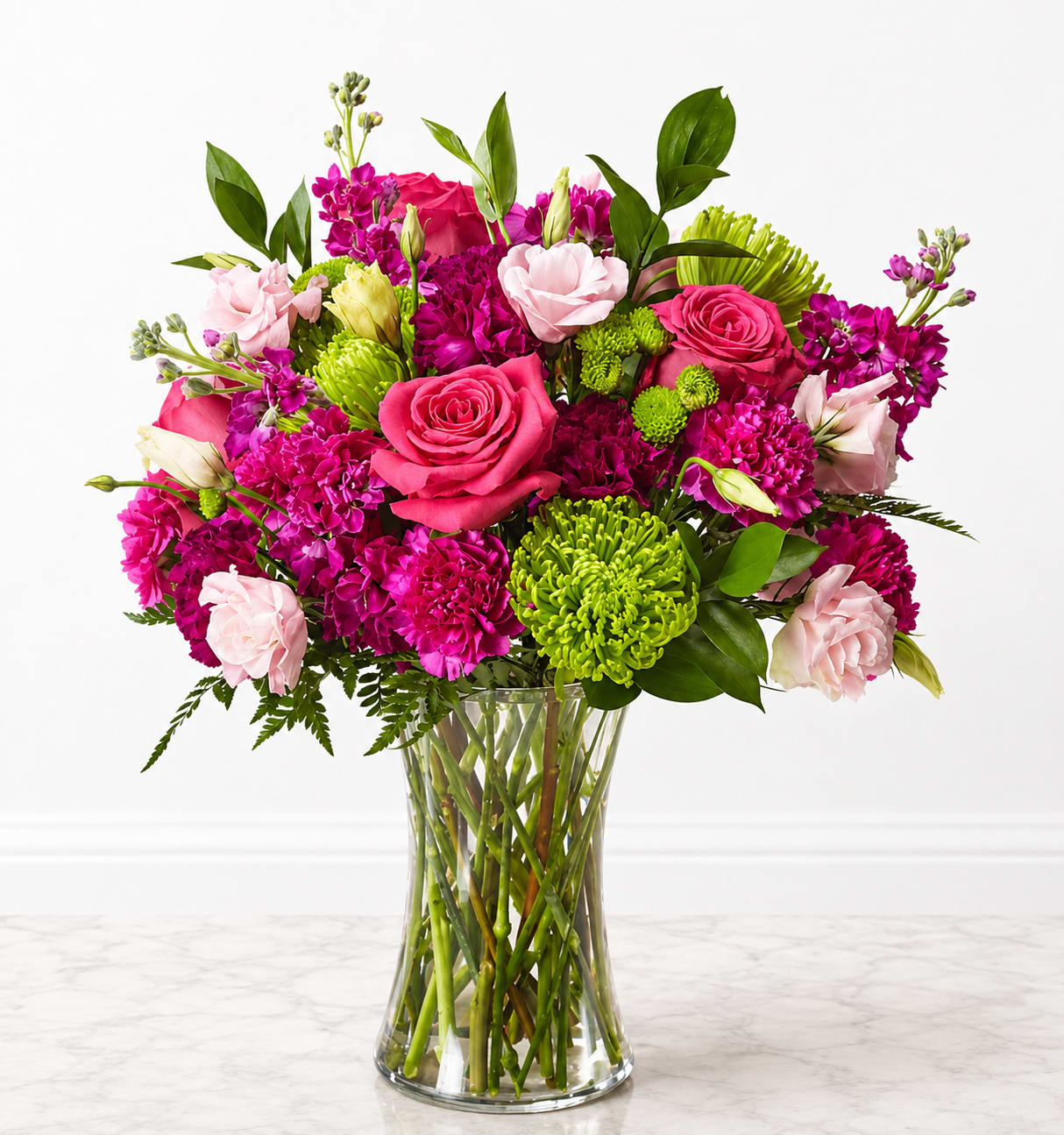  Vivid Burst of Pinks - A vivid burst of pink and magenta greets the eye - a cheerful flower arrangement perfect for birthdays, thank-yous, or brightening someone's day. This lively bouquet of roses, carnations, chrysanthemums, lisianthus, and alstroemeria reads celebratory and fresh; the mix of pinks and purples against pops of bright green creates a high-contrast, joyful look that makes the recipient feel truly celebrated.  Large roses anchor the composition while carnations and chrysanthemums add layered texture and fullness; delicate lisianthus and alstroemeria provide soft, graceful accents. Stems are arranged upright in a clear glass vase so the long, clean lines show through and the overall presentation feels polished yet effortless. Ideal for spring gifting or any moment you want to send warm, cheerful wishes - the colors and classic vase make it easy to place on a table or bedside, and basic fresh-water care will keep the blooms looking vibrant.