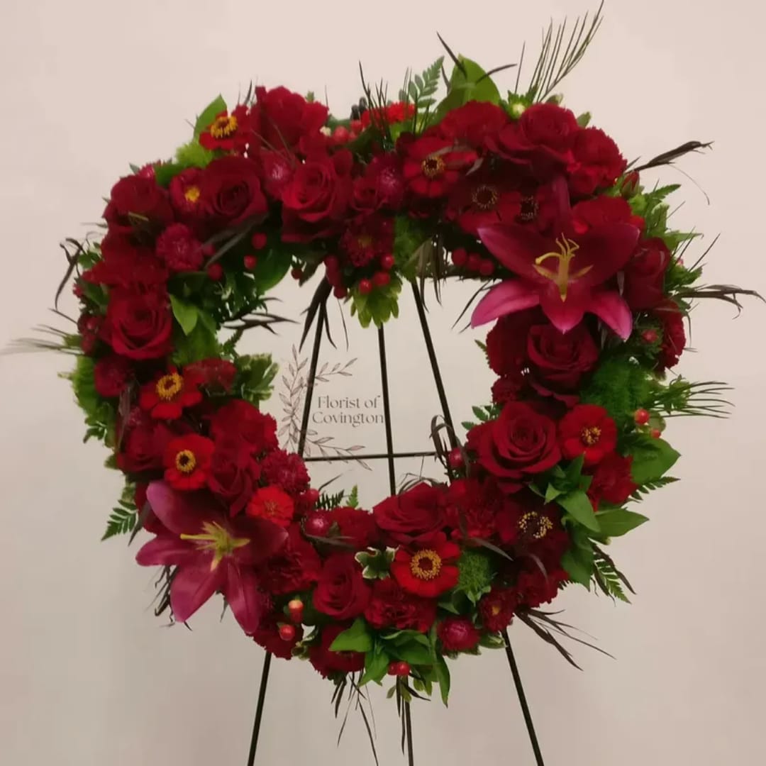 Heart-shaped floral wreath with red roses and pink lilies on a stand