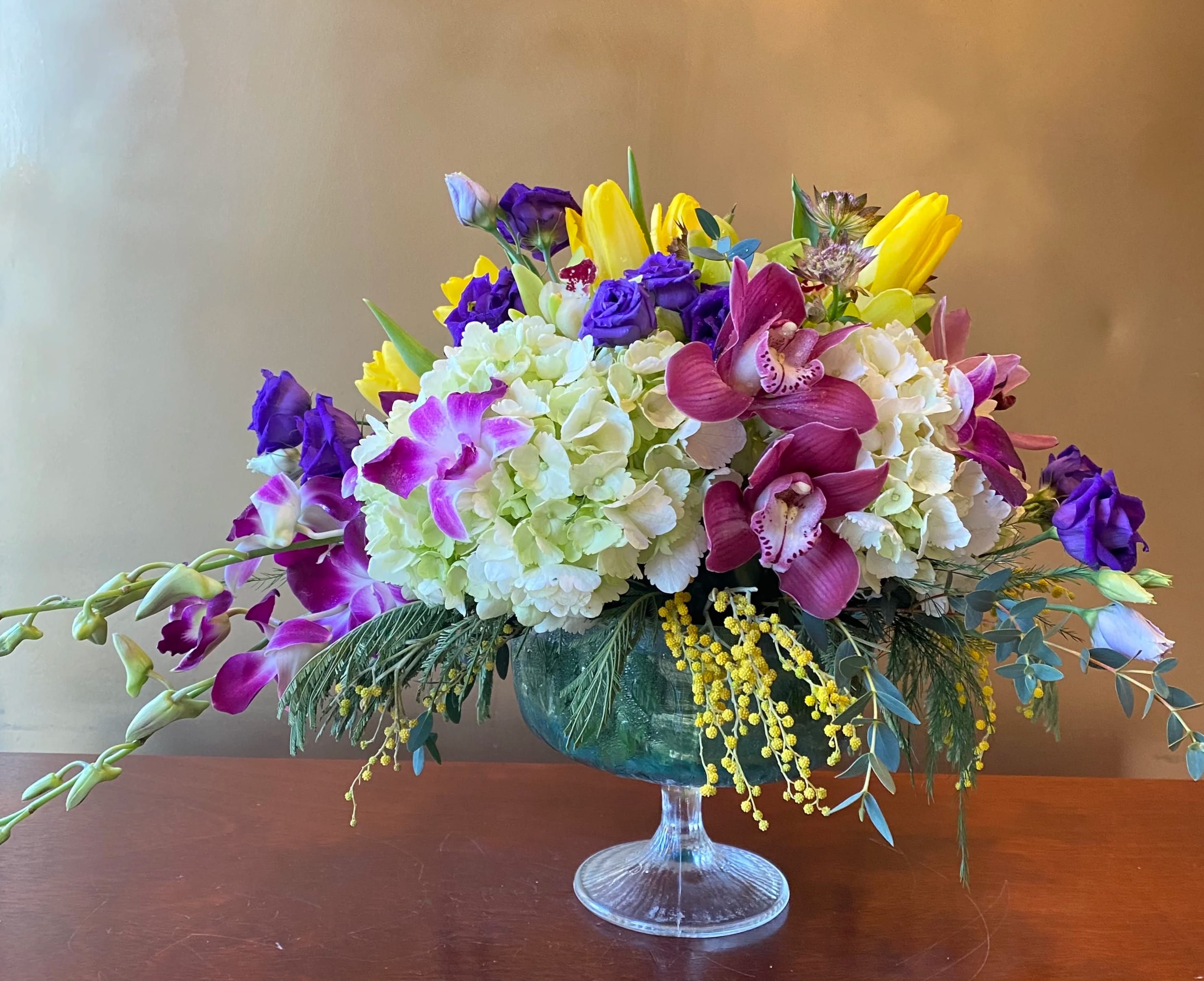 Mixed bouquet in a glass compote vase with purple, yellow, and white blooms