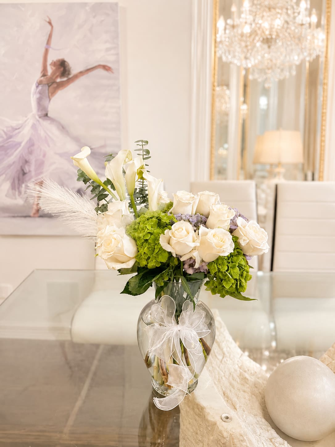 White roses and calla lilies in a glass vase with a ribbon bow