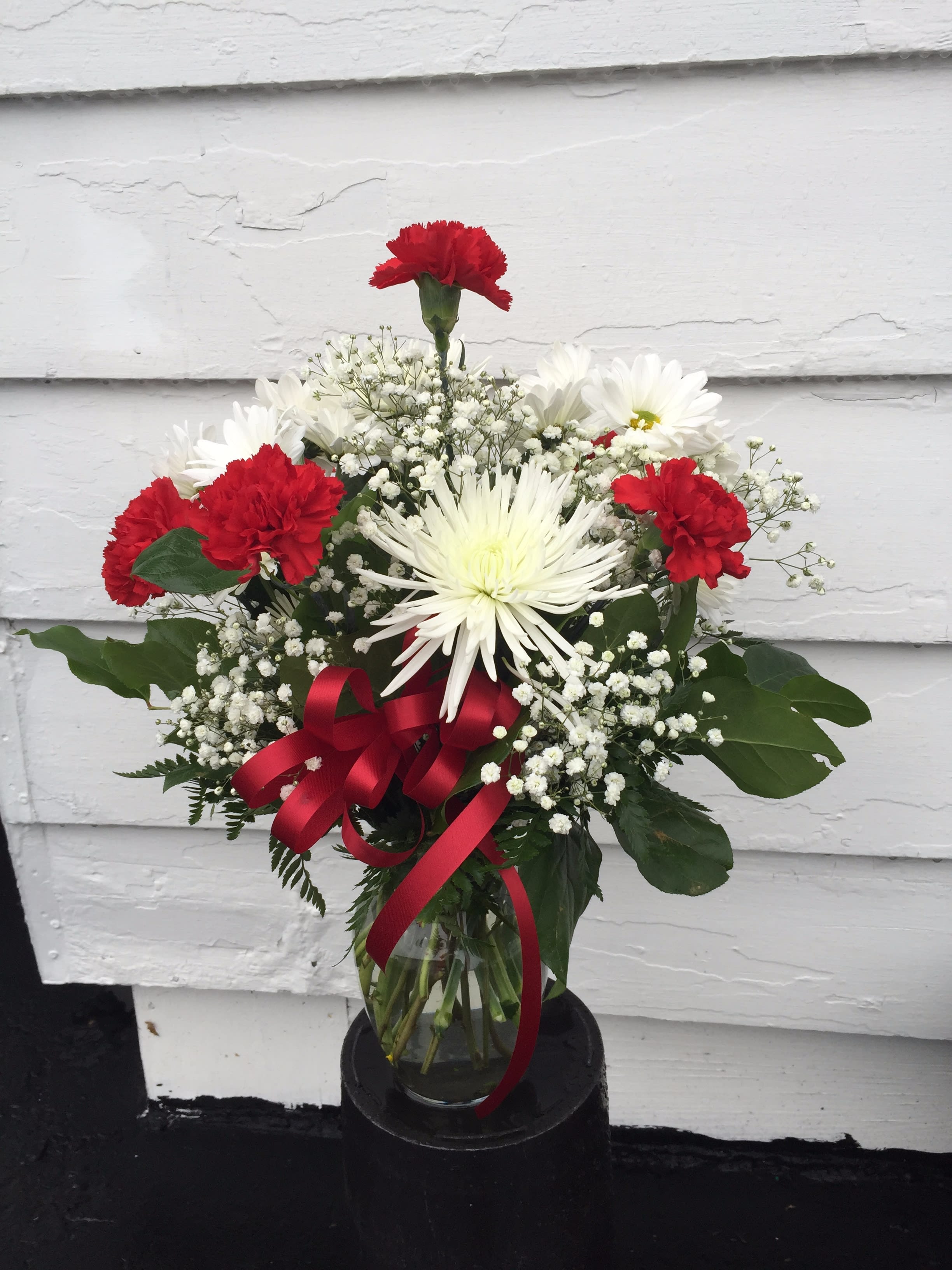 Bouquet of red carnations and white daisies in a glass vase with a red ribbon