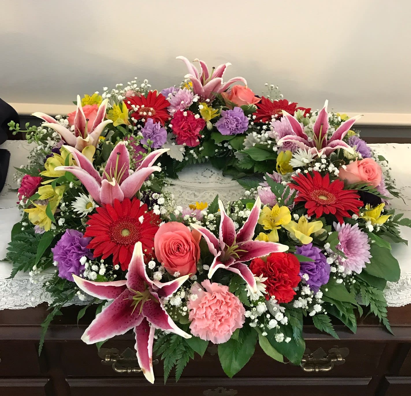 Circular floral wreath with pink lilies, red gerberas, and roses
