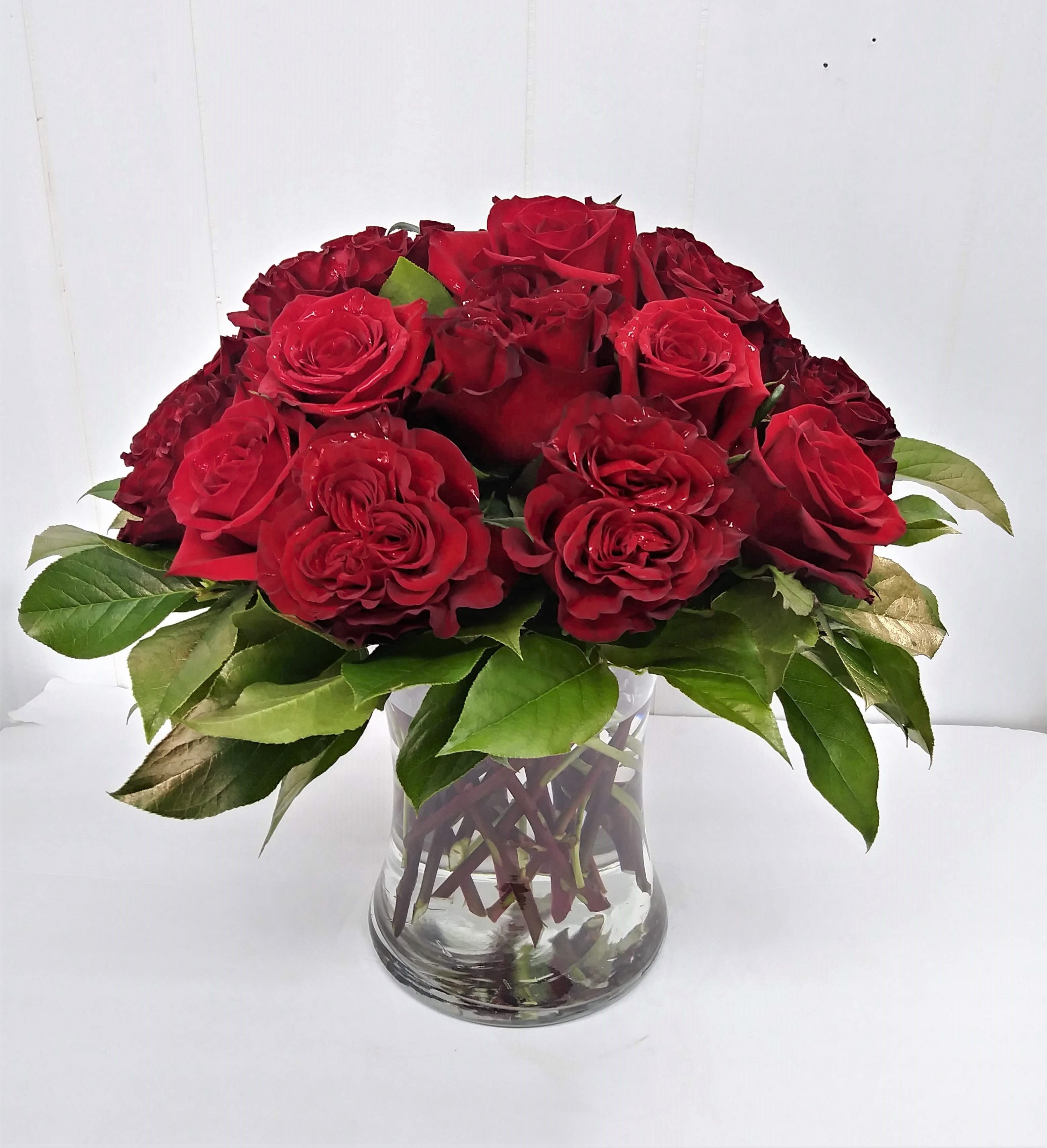 Red roses arranged in a clear glass vase with green leaves