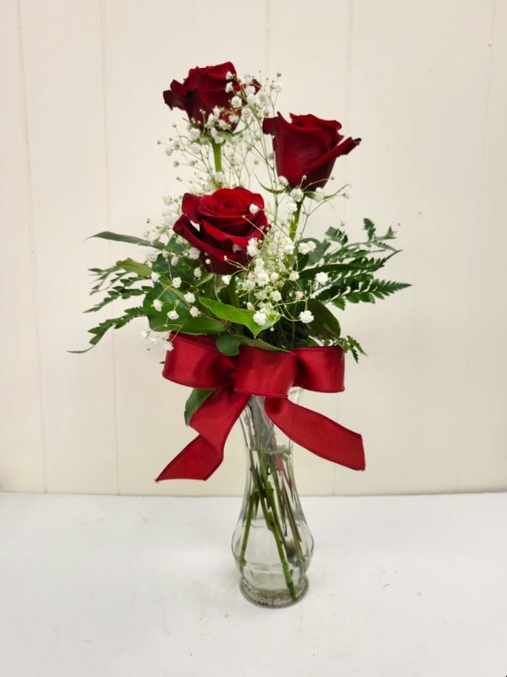Three red roses in a clear glass vase with a red ribbon