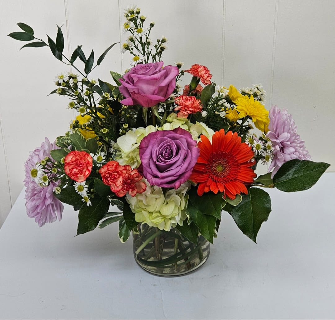 Mixed bouquet with purple roses, gerbera daisy, carnations, and hydrangea in a glass vase