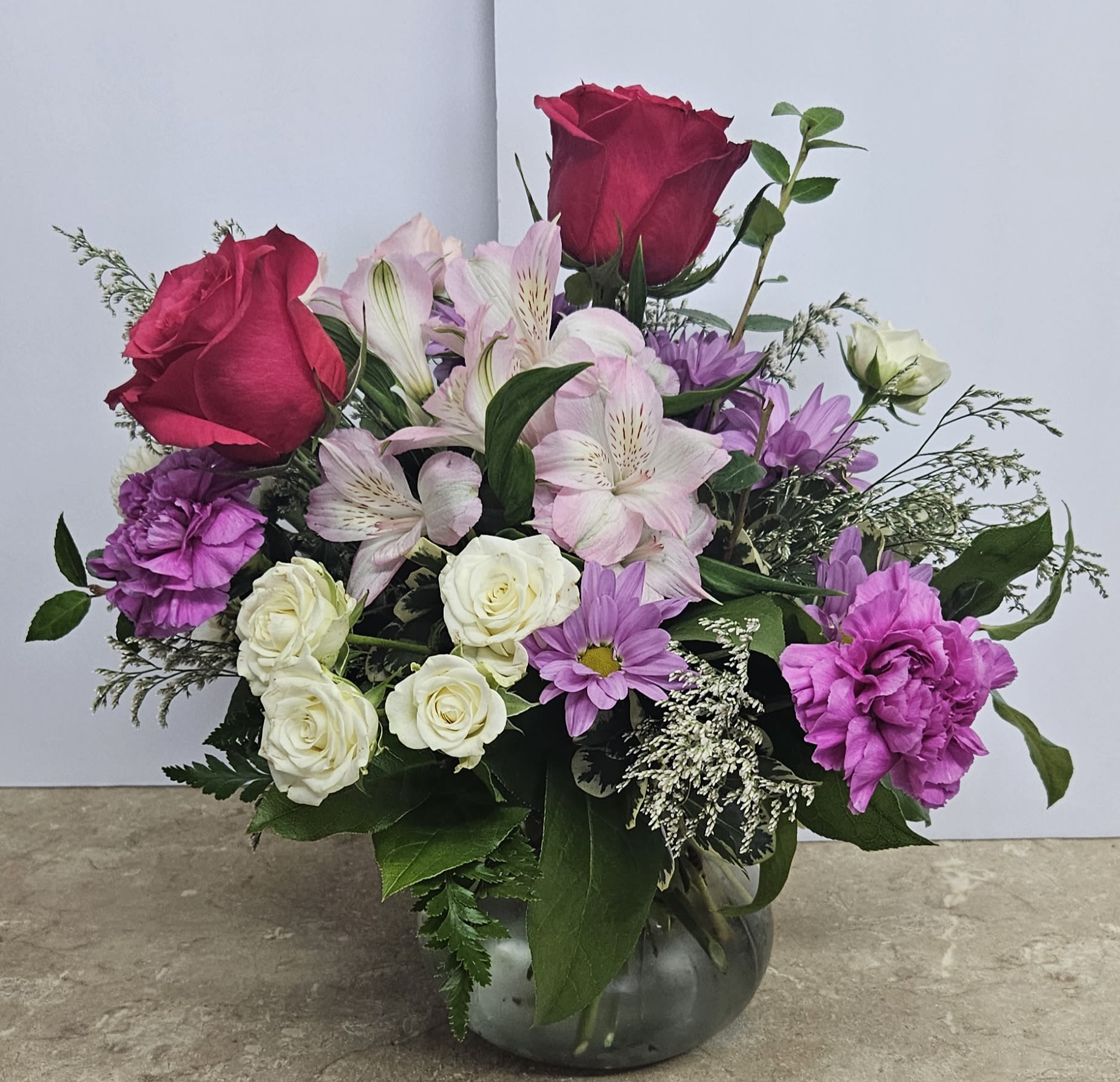 Mixed bouquet of roses, lilies, and purple flowers in a glass vase