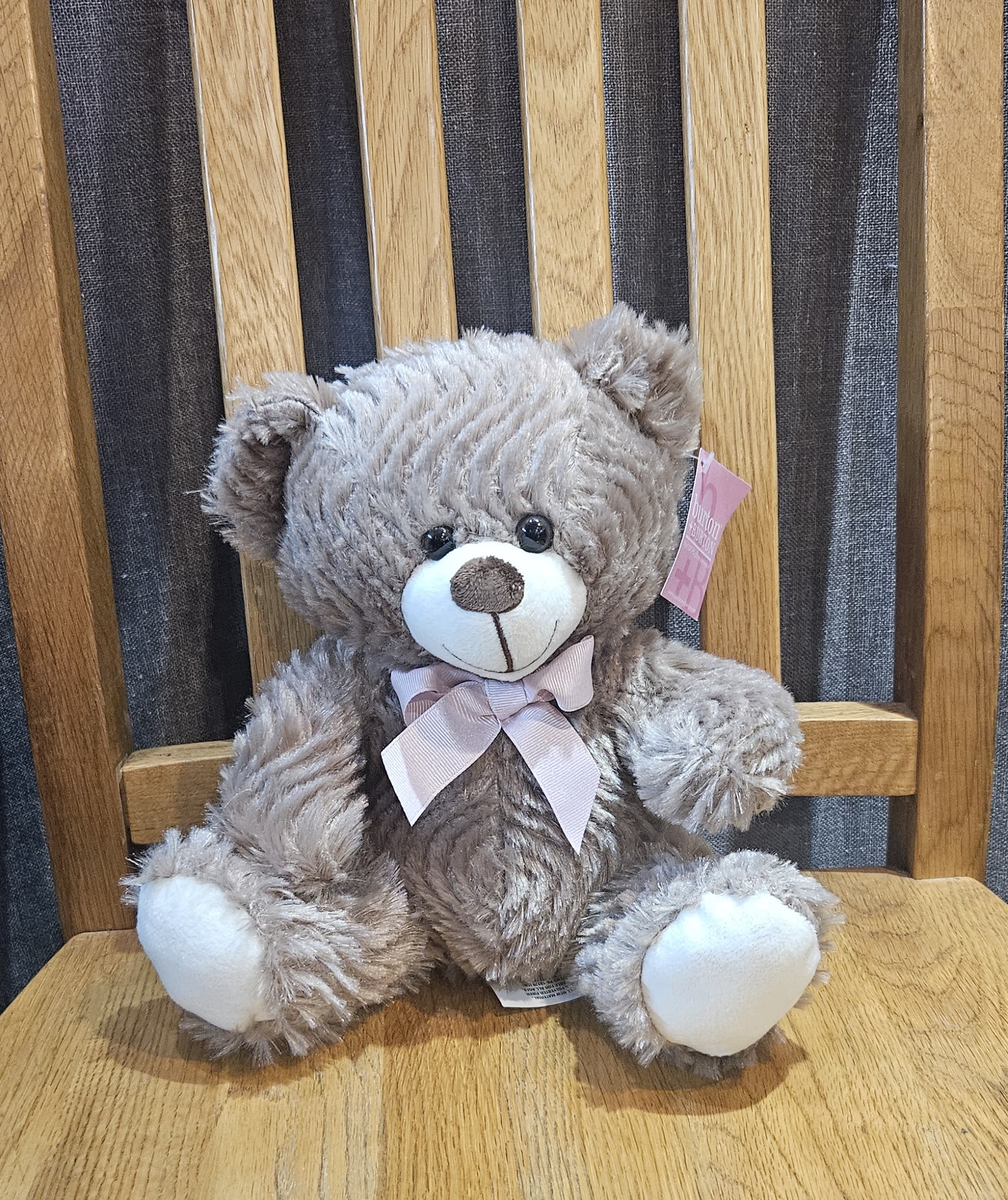 Gray teddy bear with a pink ribbon sitting on a wooden chair