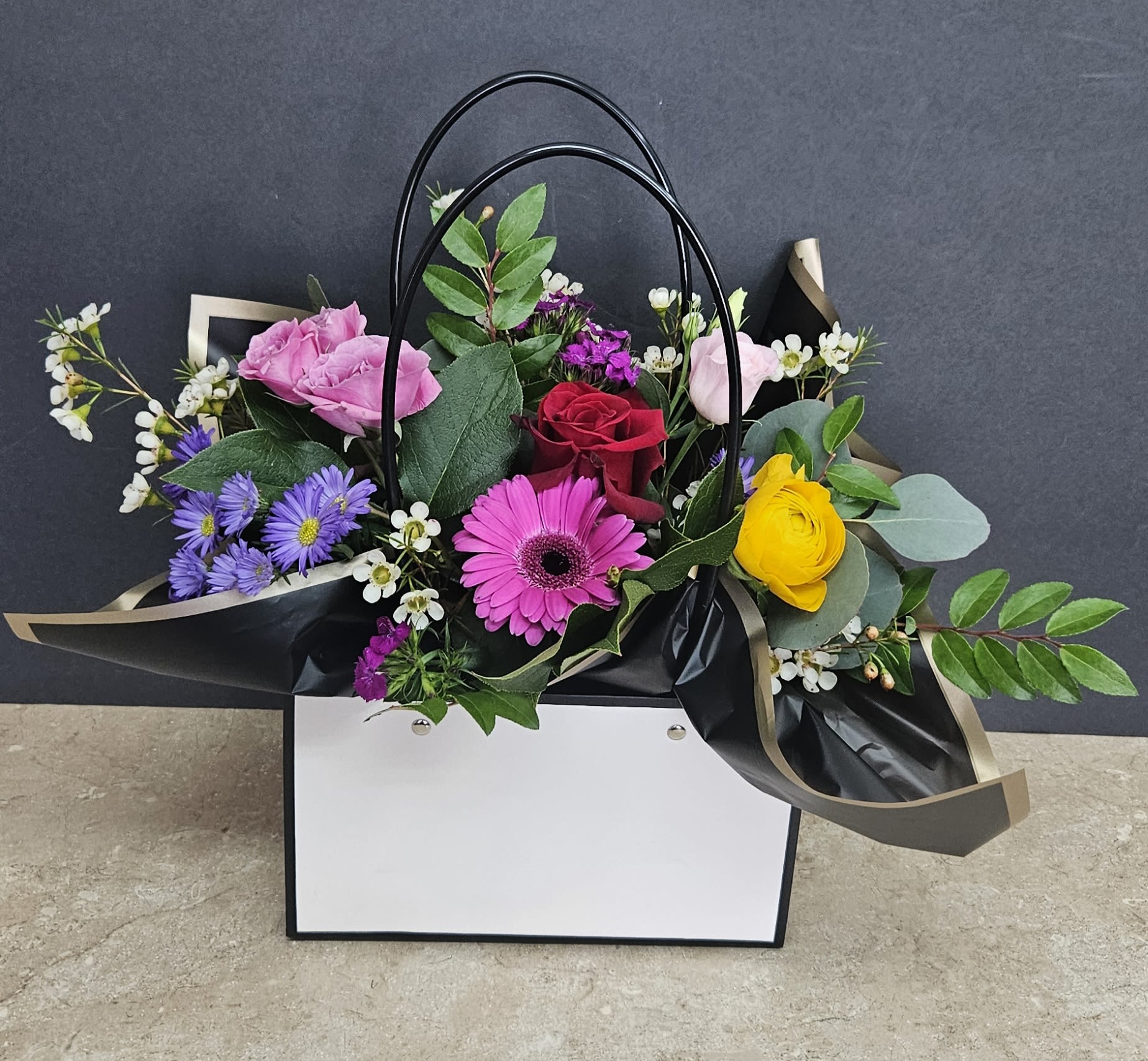 Mixed bouquet in a black handled gift bag with pink, red, yellow, and purple flowers