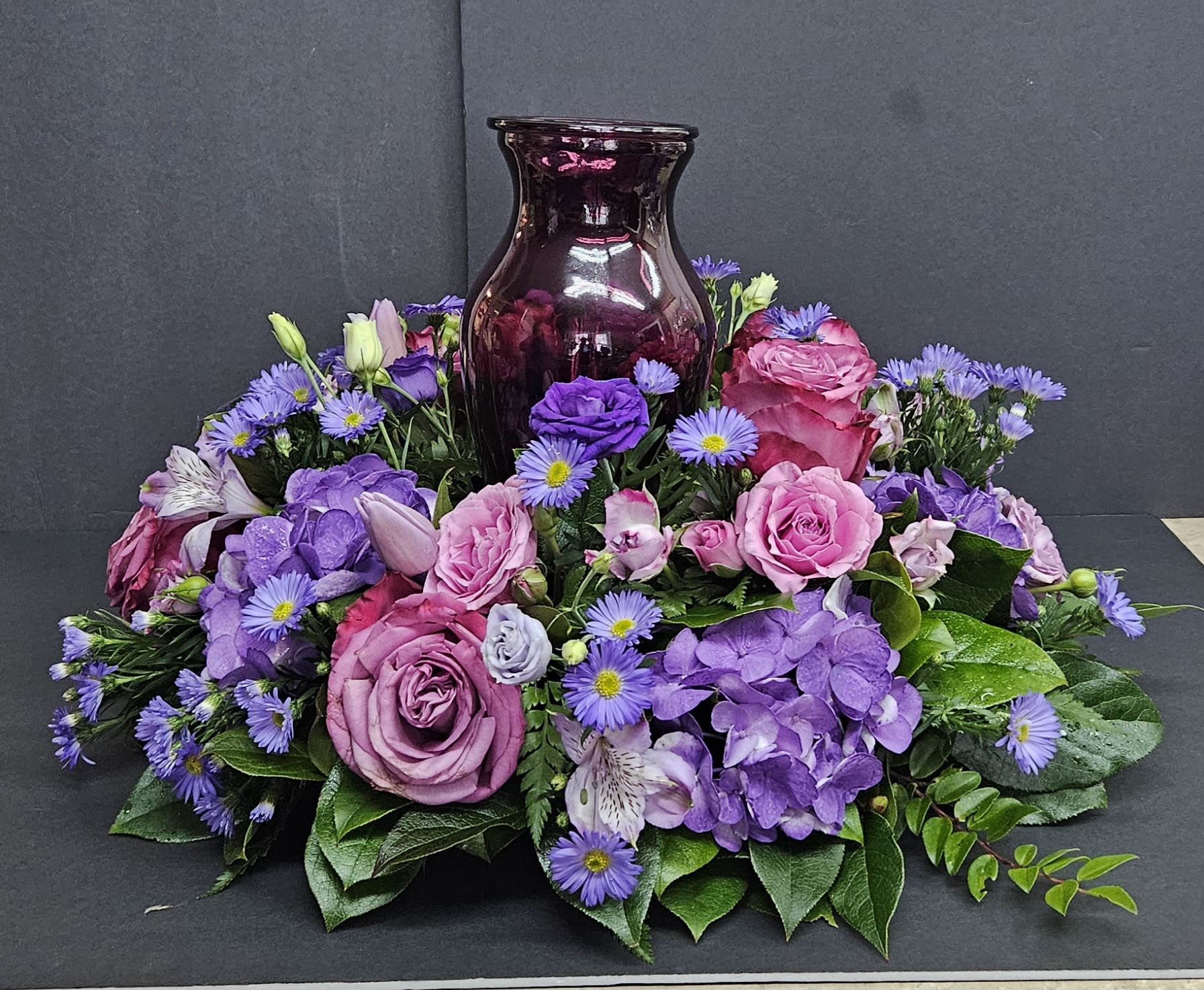 Purple and pink floral arrangement around a dark glass vase