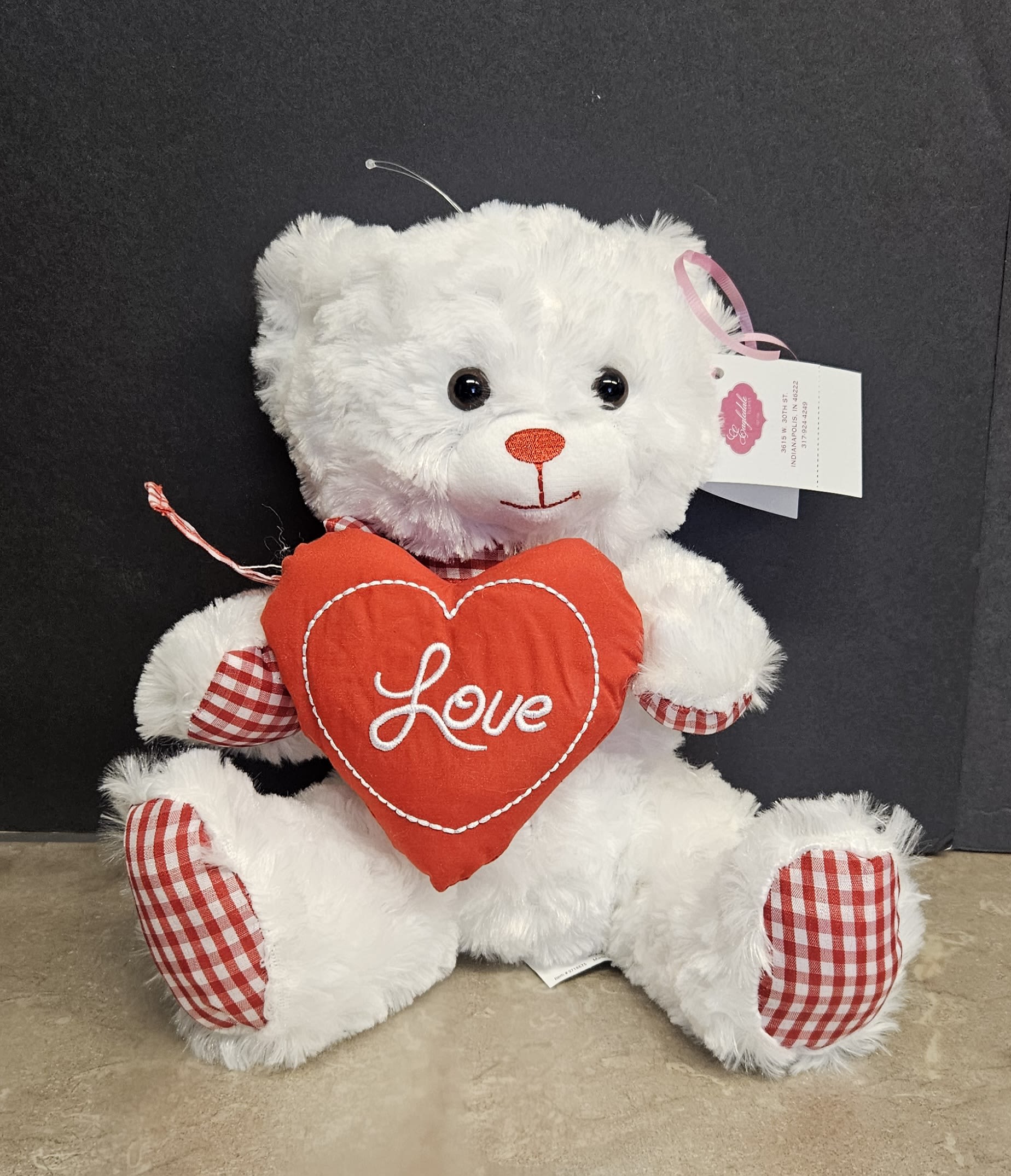 White teddy bear holding a red heart pillow with the word Love