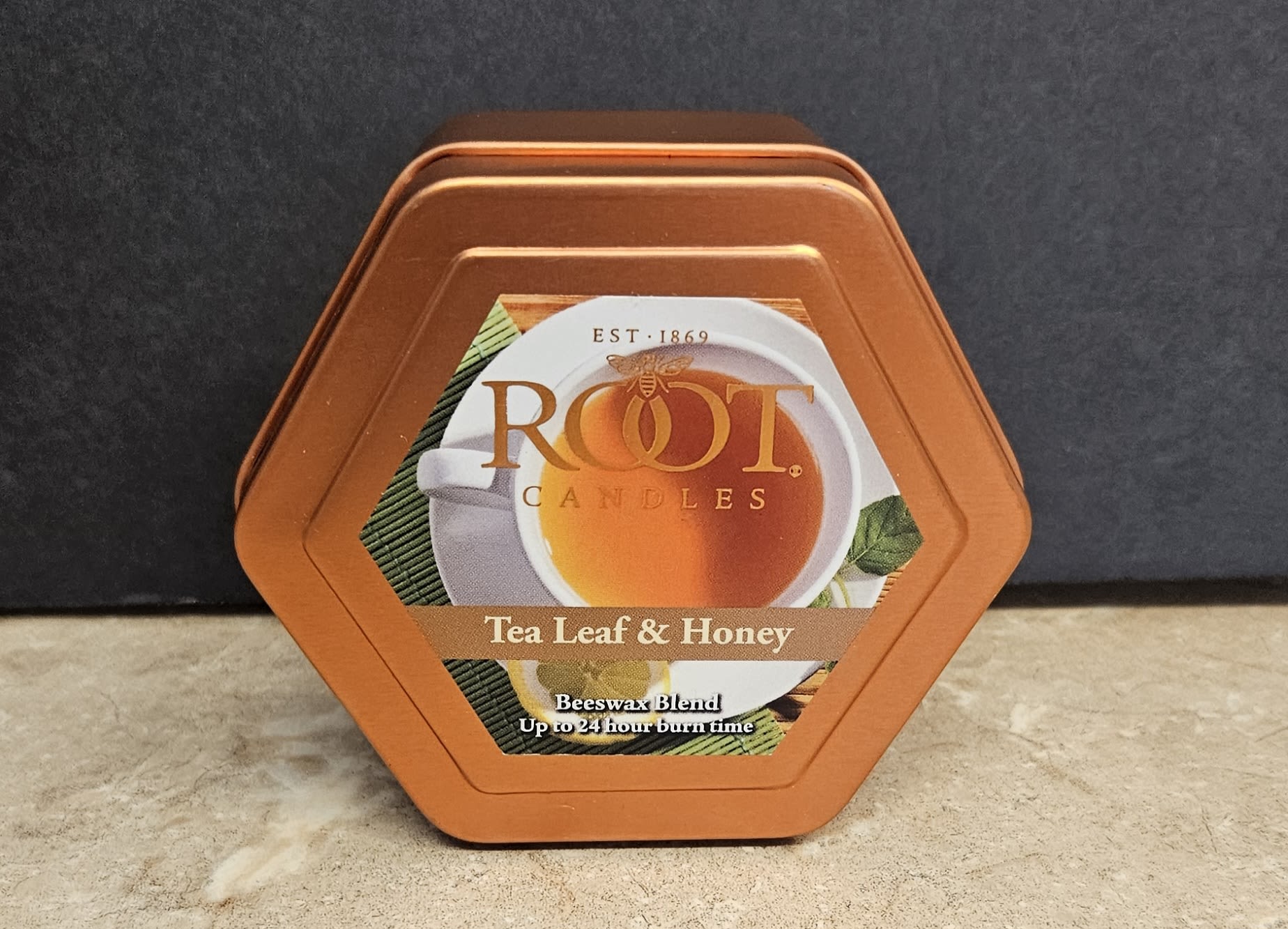 Root Candle Tea leaf &amp; Honey Tin S - A cozy, giftable tea-scented candle tin that brings warm, comforting fragrance to any room - perfect as a small everyday gift or an accompaniment to a thoughtful bouquet for a housewarming or birthday. This flower arrangement page pairs this Root Candle Tea Leaf &amp; Honey metal tin with arrangements, so mention it as a complement when you're sending flowers for occasions like thank-you gestures, seasonal comfort, or a cheerful pick-me-up for someone who loves subtle, tea-inspired scents.  The candle comes in a hexagonal orange metal tin with a clean printed label showing a steaming cup of tea, conveying a homely, comforting vibe. Colors on the packaging read orange, white, black, and green; the compact size and neat retail presentation make it easy to tuck alongside a dozen roses or a mixed seasonal arrangement. Include it as a finishing touch at checkout to make the recipient feel cozy and cared for - no special care required for the tin itself; it's ready to gift straight from the shop.