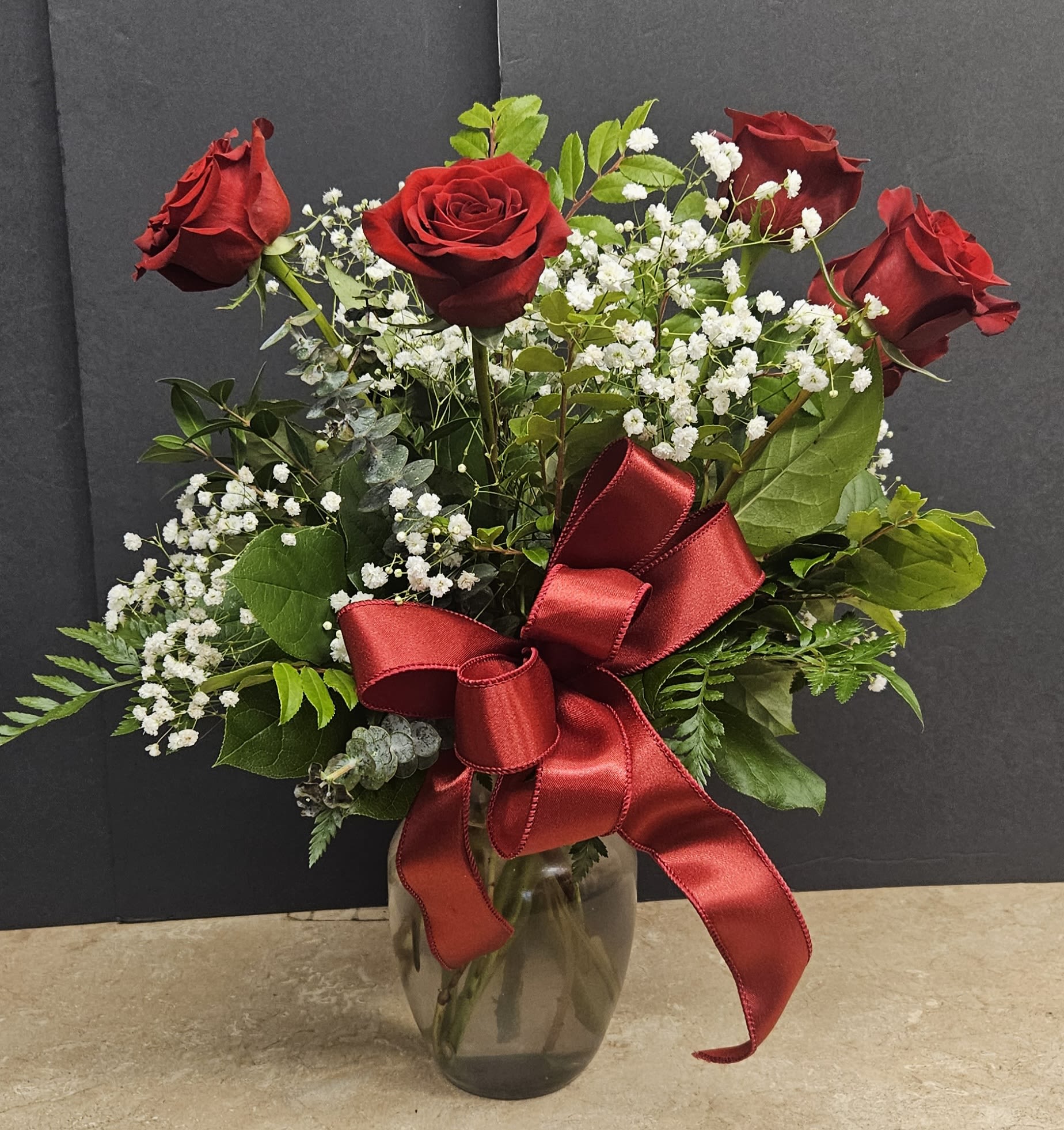 Red roses with baby's breath in a glass vase and red ribbon