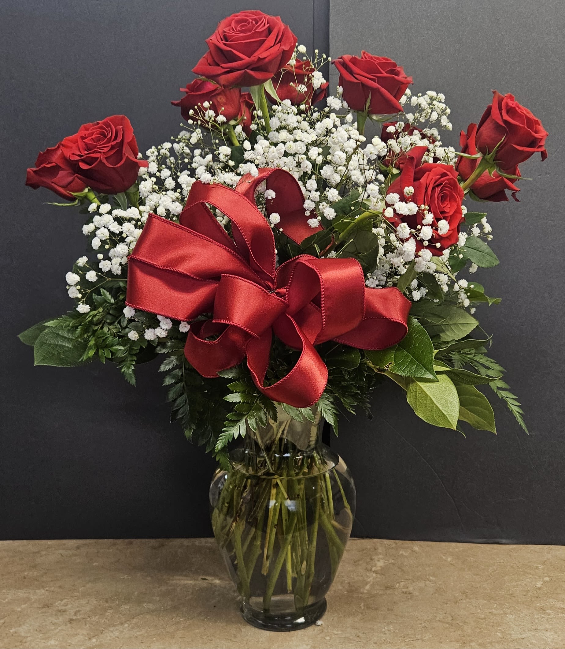 Red roses with baby's breath in a glass vase and red ribbon