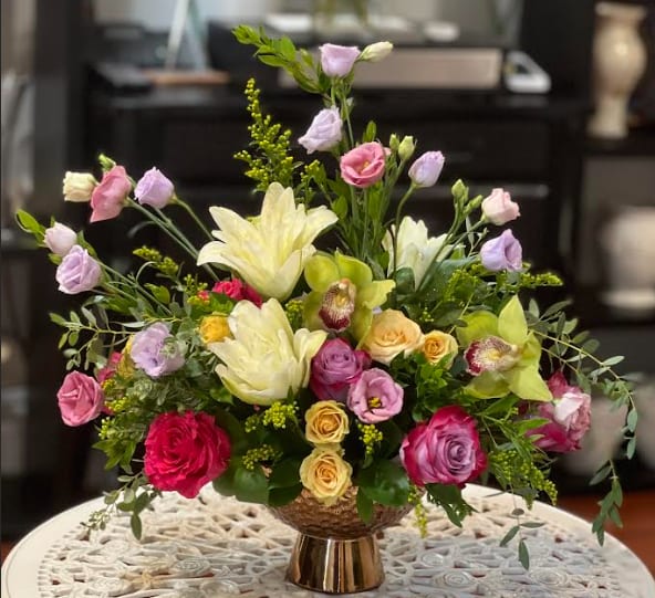 Mixed bouquet of roses, lilies, and lisianthus in a gold vase