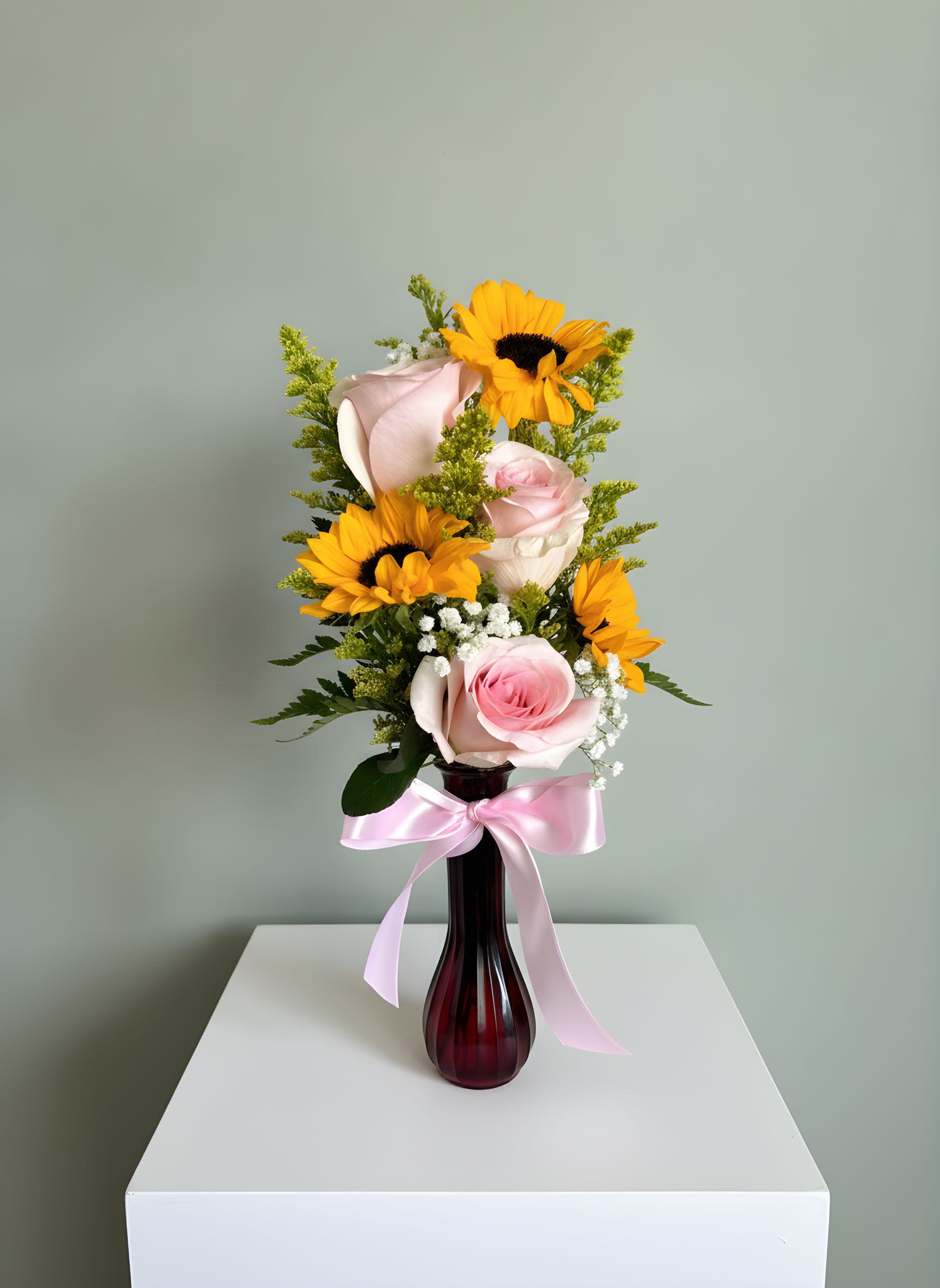 Pink Rose &amp; Sunflower Vase Arrangement - Bright, cheerful, and full of charm, this elegant vase arrangement features soft pink roses paired with vibrant sunflowers, accented with baby's breath and fresh greenery. Designed in a sleek glass vase and finished with a delicate satin ribbon, this arrangement creates the perfect balance of warmth and elegance.  Whether you're celebrating a birthday, sending a thoughtful thank-you, welcoming a new baby, or simply brightening someone's day, this design delivers a beautiful and uplifting message.  Includes:  Premium pink roses Fresh sunflowers Baby's breath accents Seasonal greenery Decorative glass vase with ribbon  Flower shades and vase style may vary slightly based on seasonal availability while maintaining the overall look and value of the arrangement. 