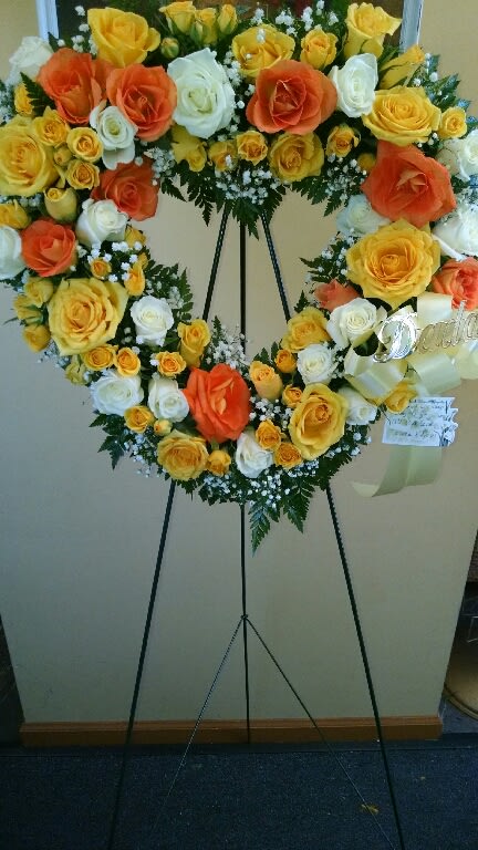Heart-shaped rose wreath on an easel with yellow, orange, and white blooms