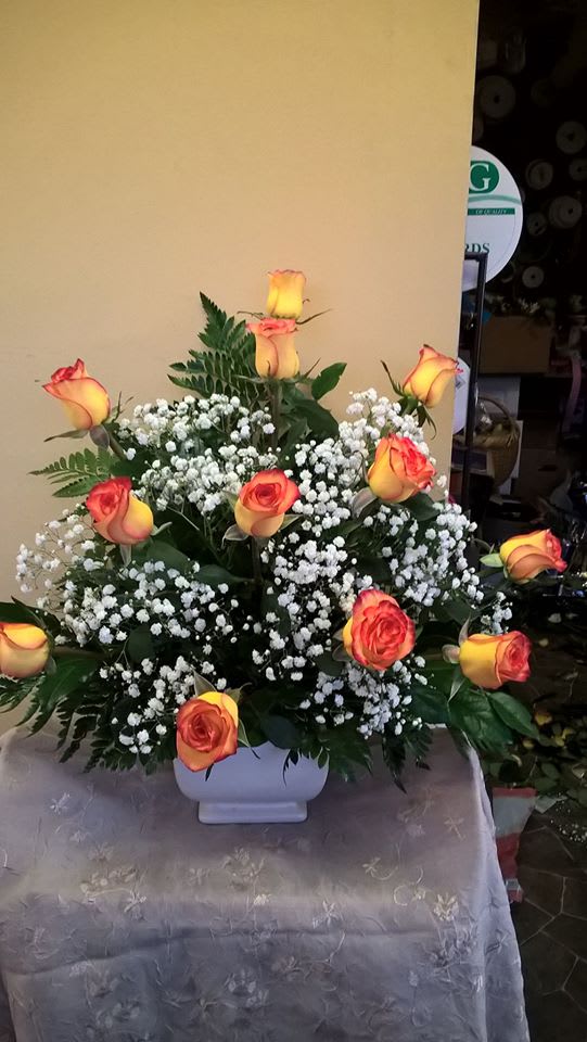 Orange-yellow roses arranged in a white vase with baby's breath