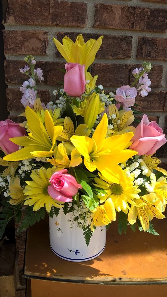 Yellow lilies and pink roses arranged in a white vase
