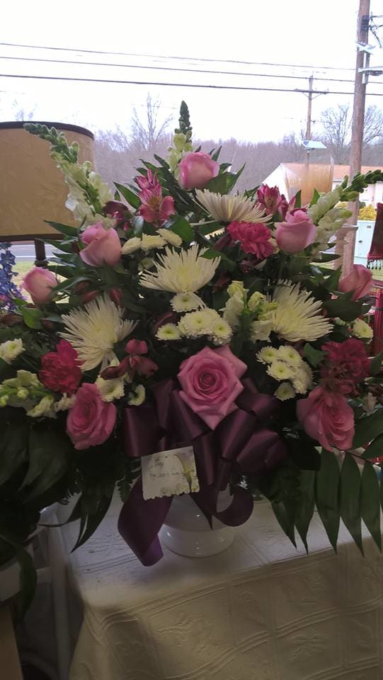 Pink roses and white spider mums arranged in a vase with a purple ribbon.