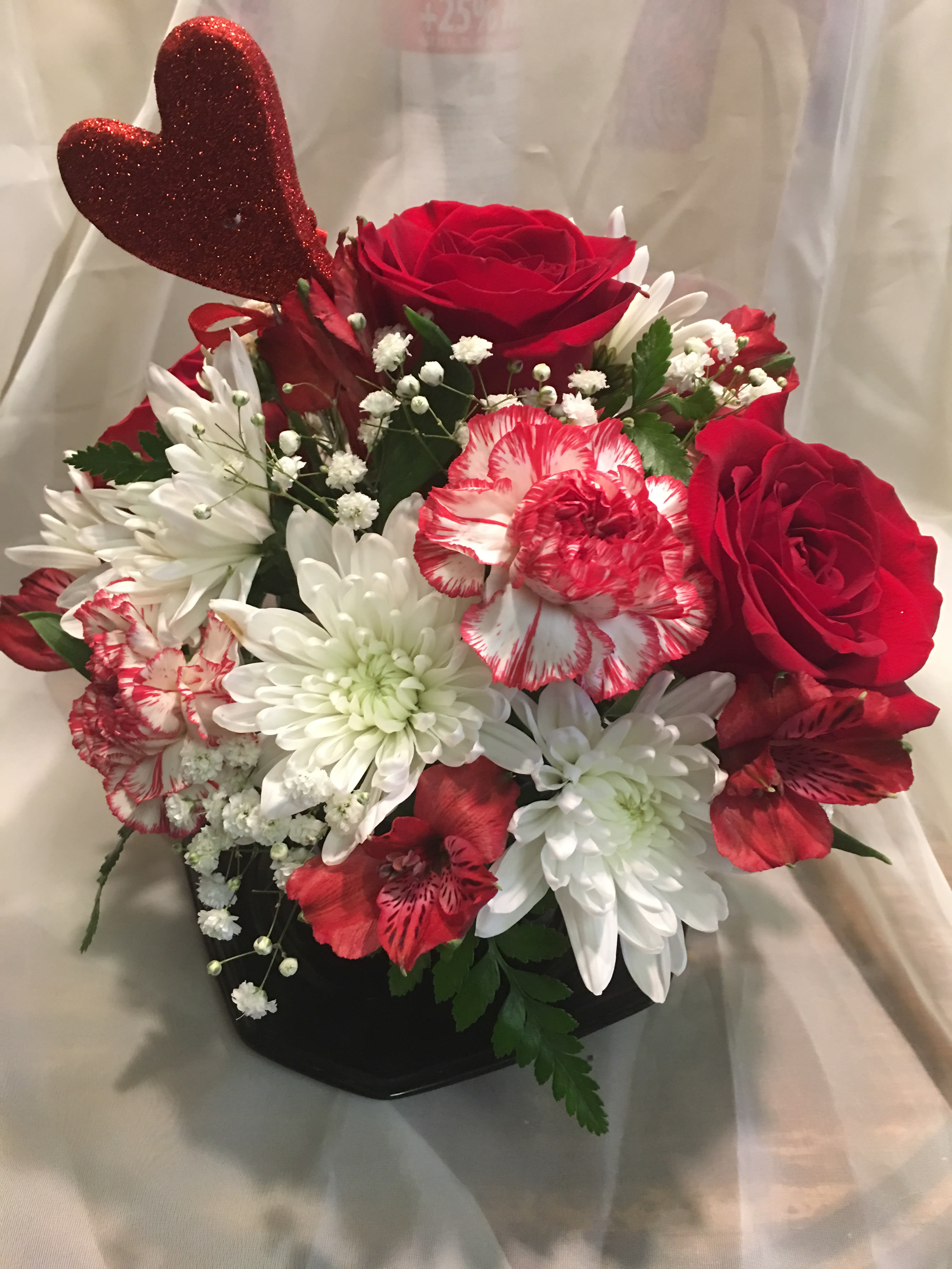 Red roses and white daisies in a black vase with a glitter heart pick