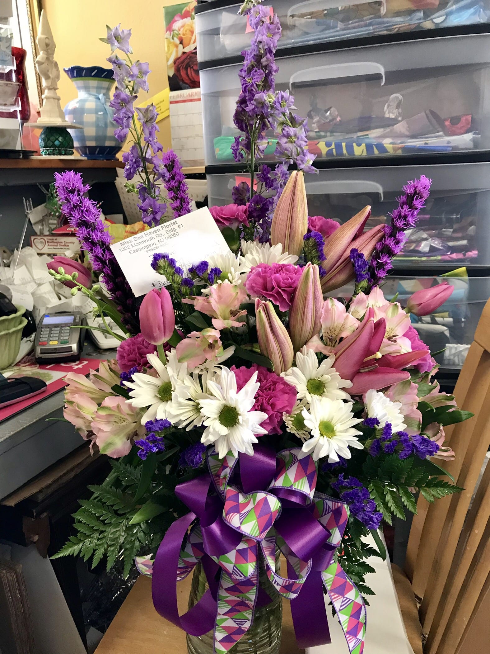Pink and white mixed bouquet in a glass vase with purple ribbon