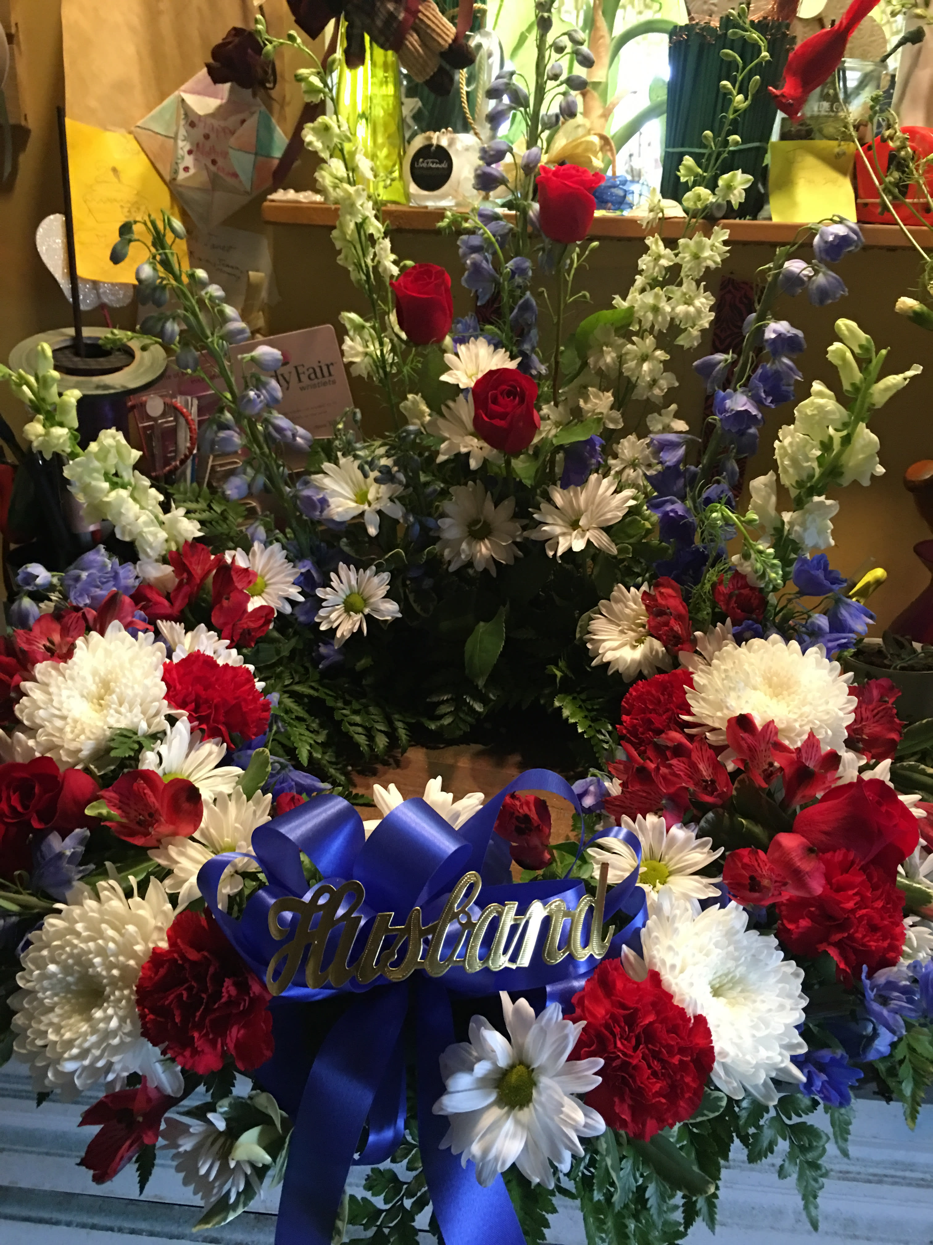 Floral arrangement with red roses, white daisies, and blue flowers with a blue ribbon