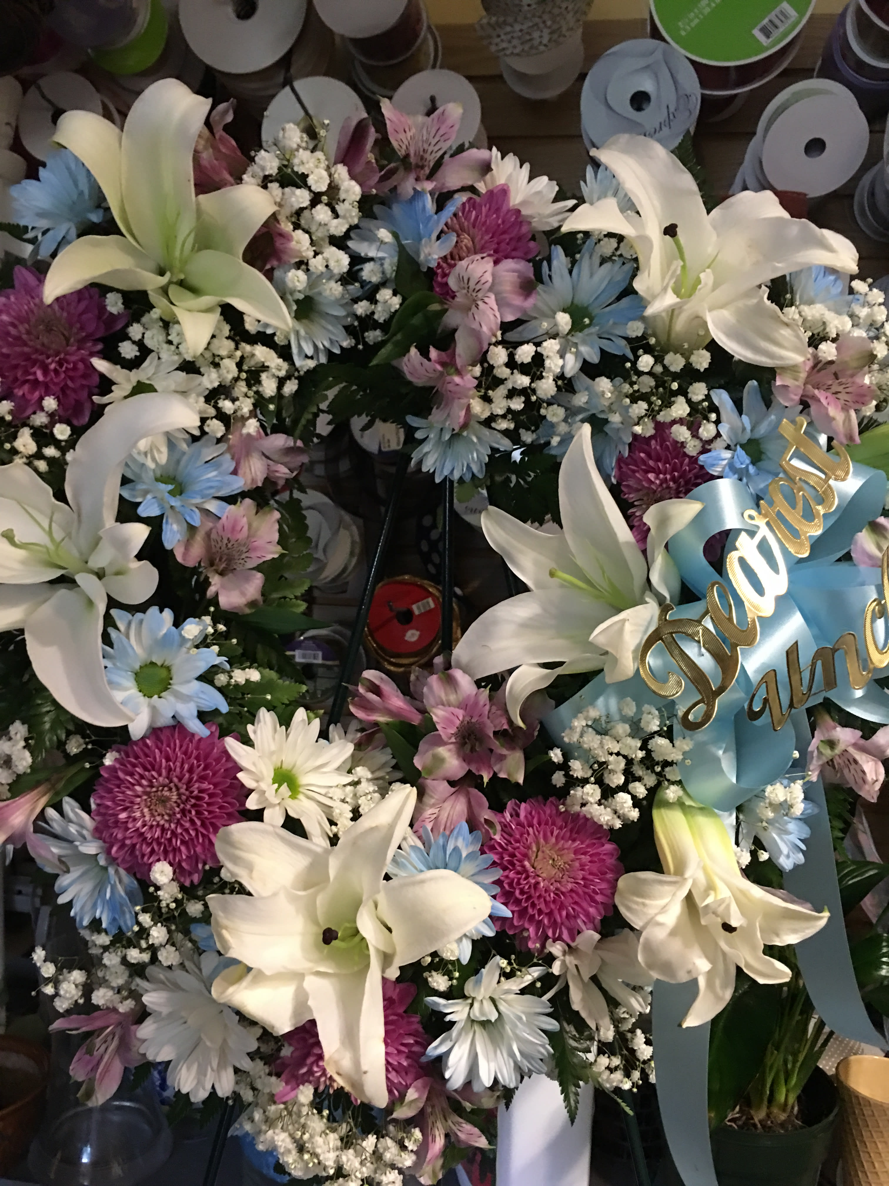 Floral wreath with white lilies, purple and blue daisies, and a blue ribbon