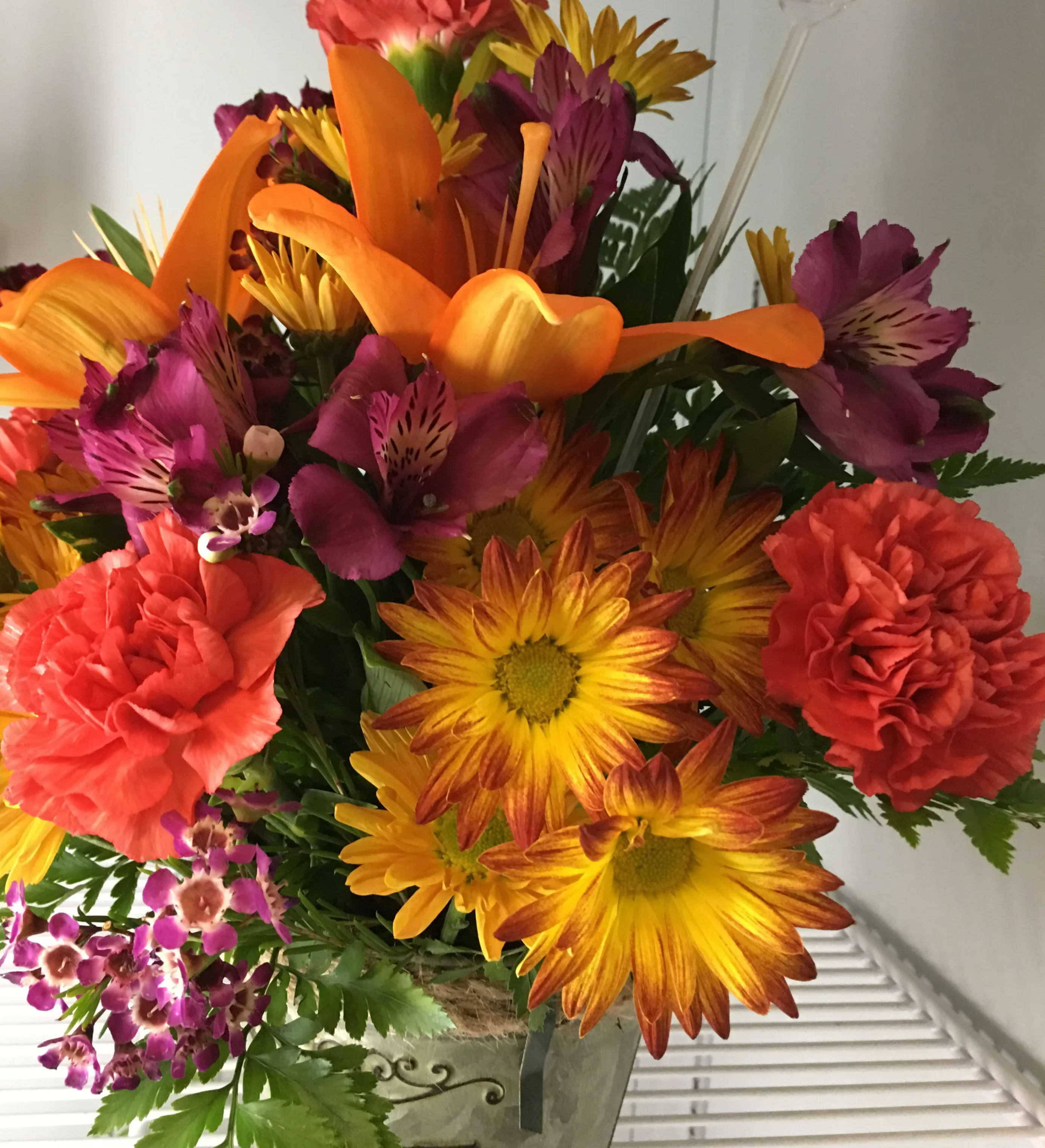 Fall Fields - Capturing all the colors of fall will warm the hearts, this one-sided arrangement is a perfect way to wish them well or say Happy Birthday. A lily sits amidst daisies, carnations, and alstromeria. in one of our many containers (colors may vary).    