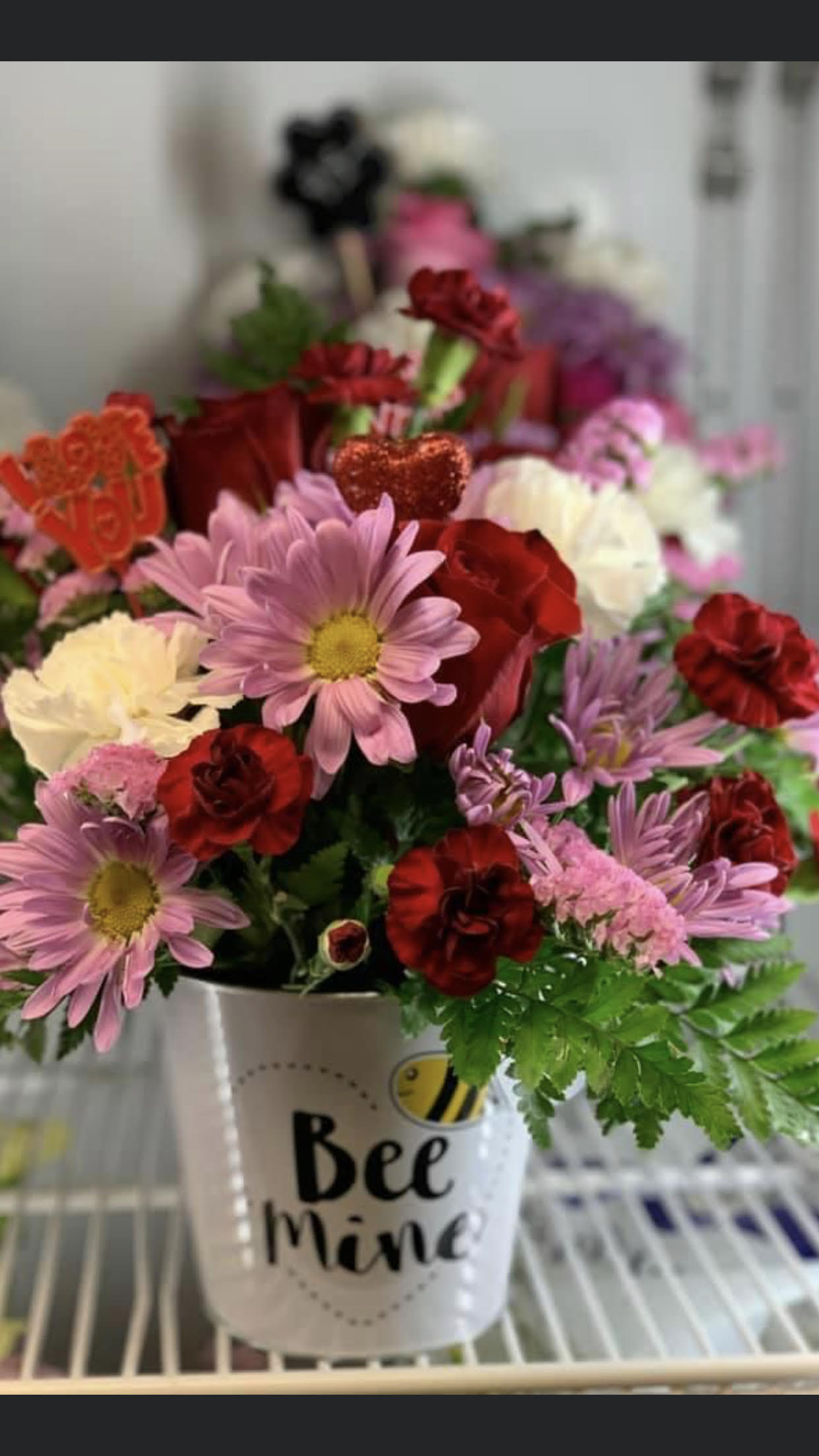 Mixed pink, red, and white flowers in a white "Bee Mine" container