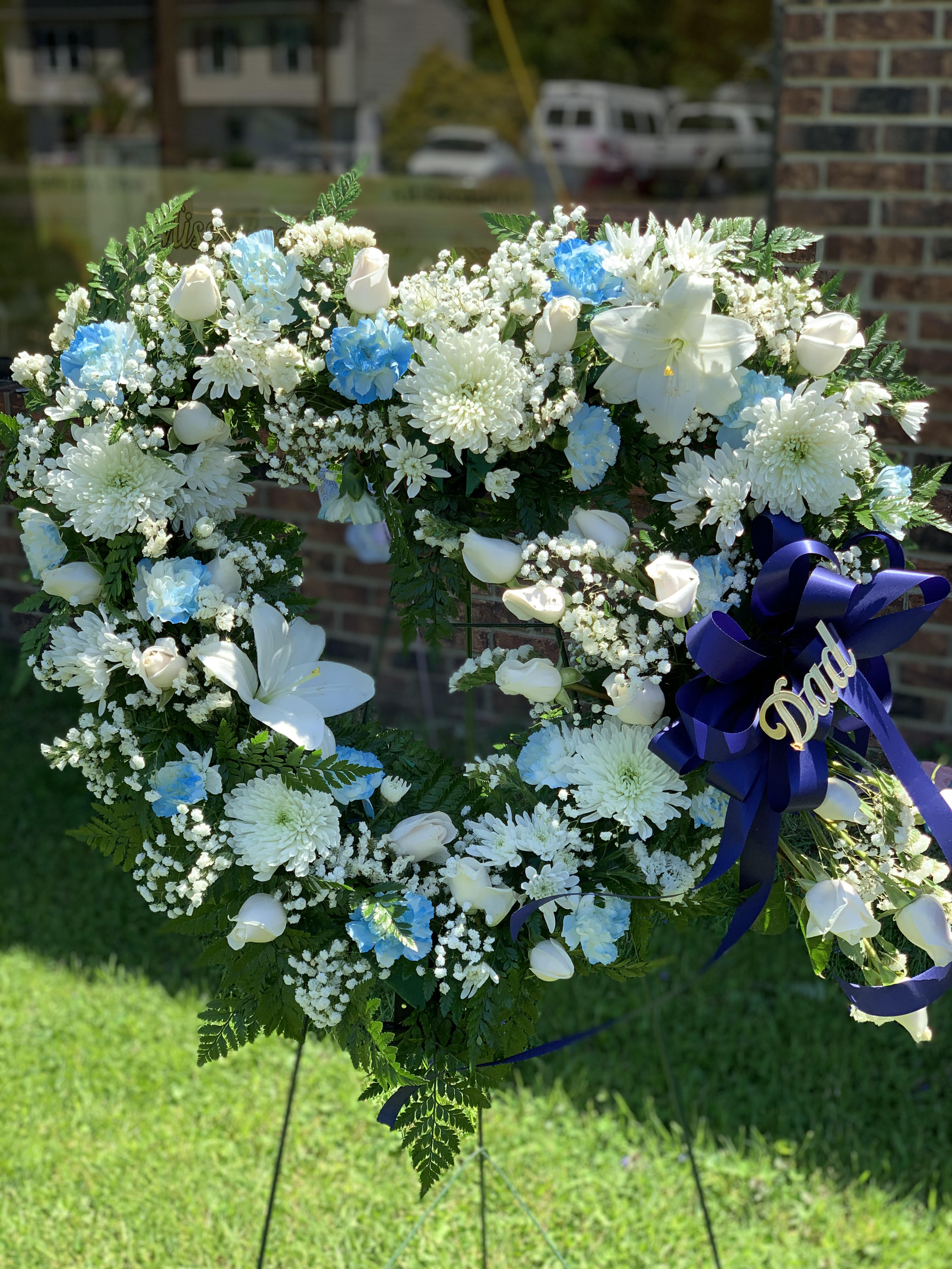 Heart-shaped white floral wreath with blue accents and a purple ribbon