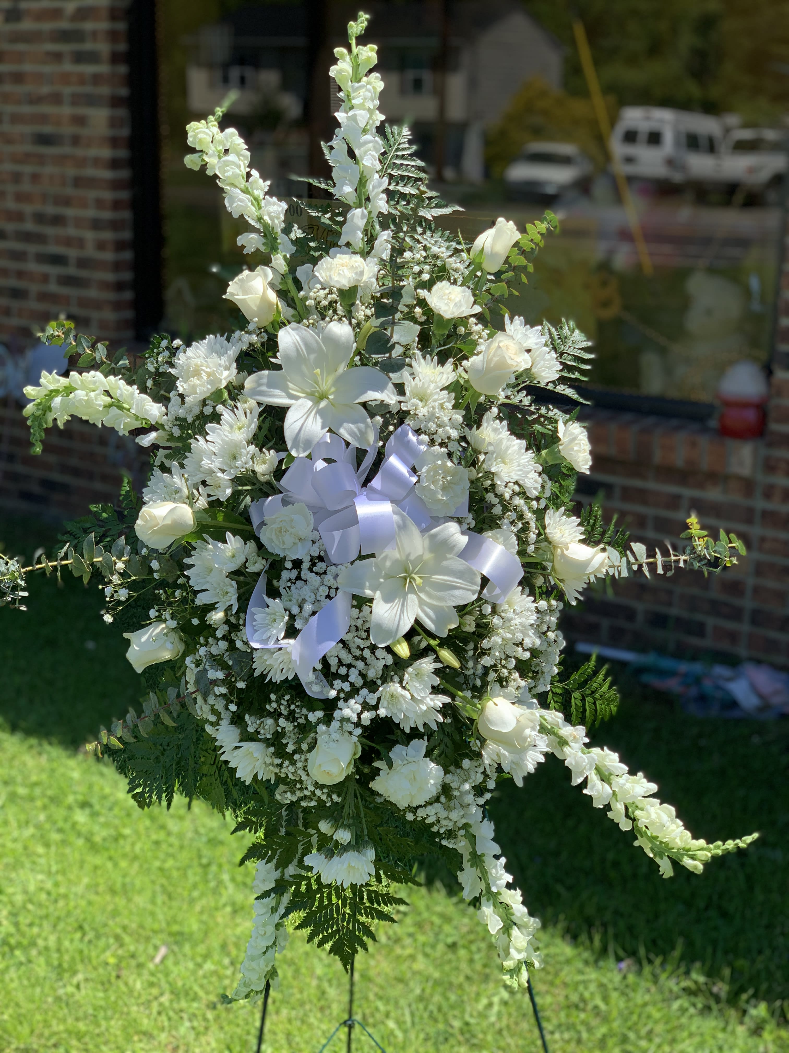 White funeral spray with lilies, roses, and ribbon on a stand