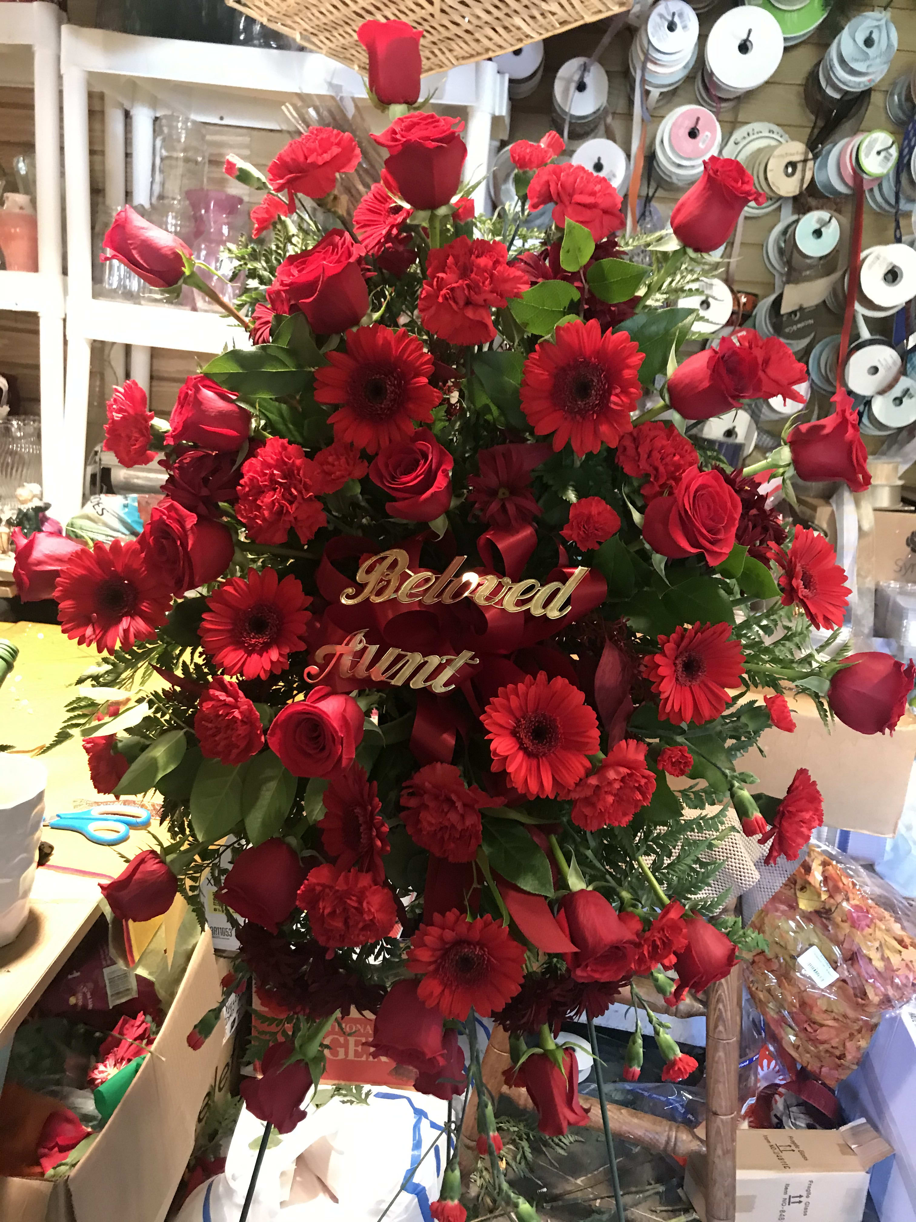 Red roses and gerbera daisies arranged in a standing spray with a "Beloved Aunt" sign.