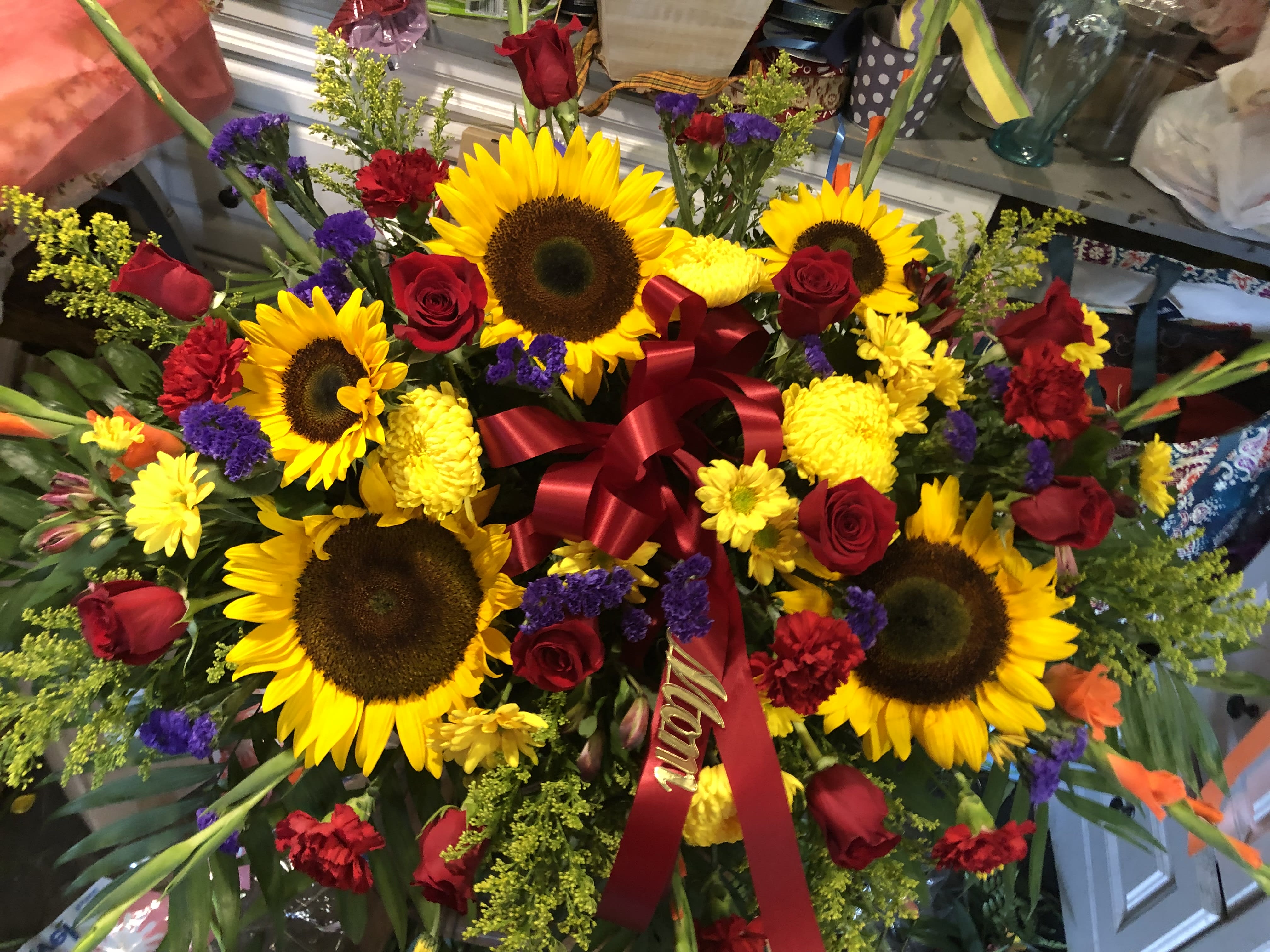 Large bouquet of sunflowers, red roses, and yellow flowers with a red ribbon