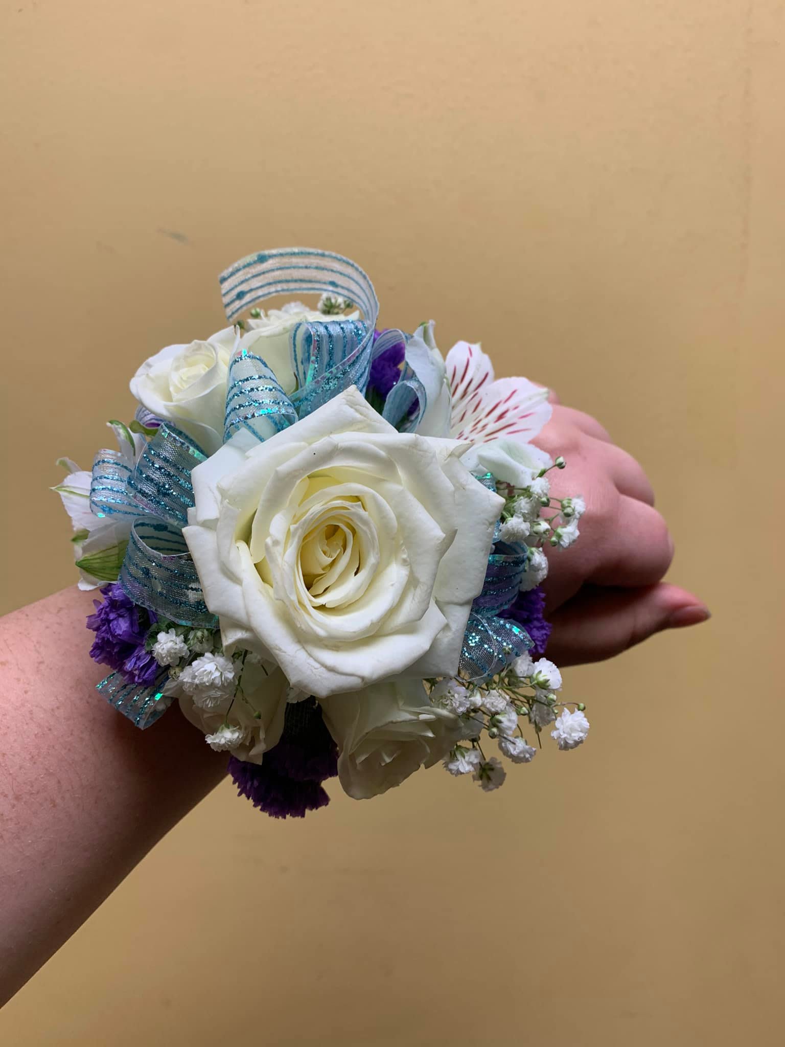 White rose wrist corsage with blue ribbon and purple accents