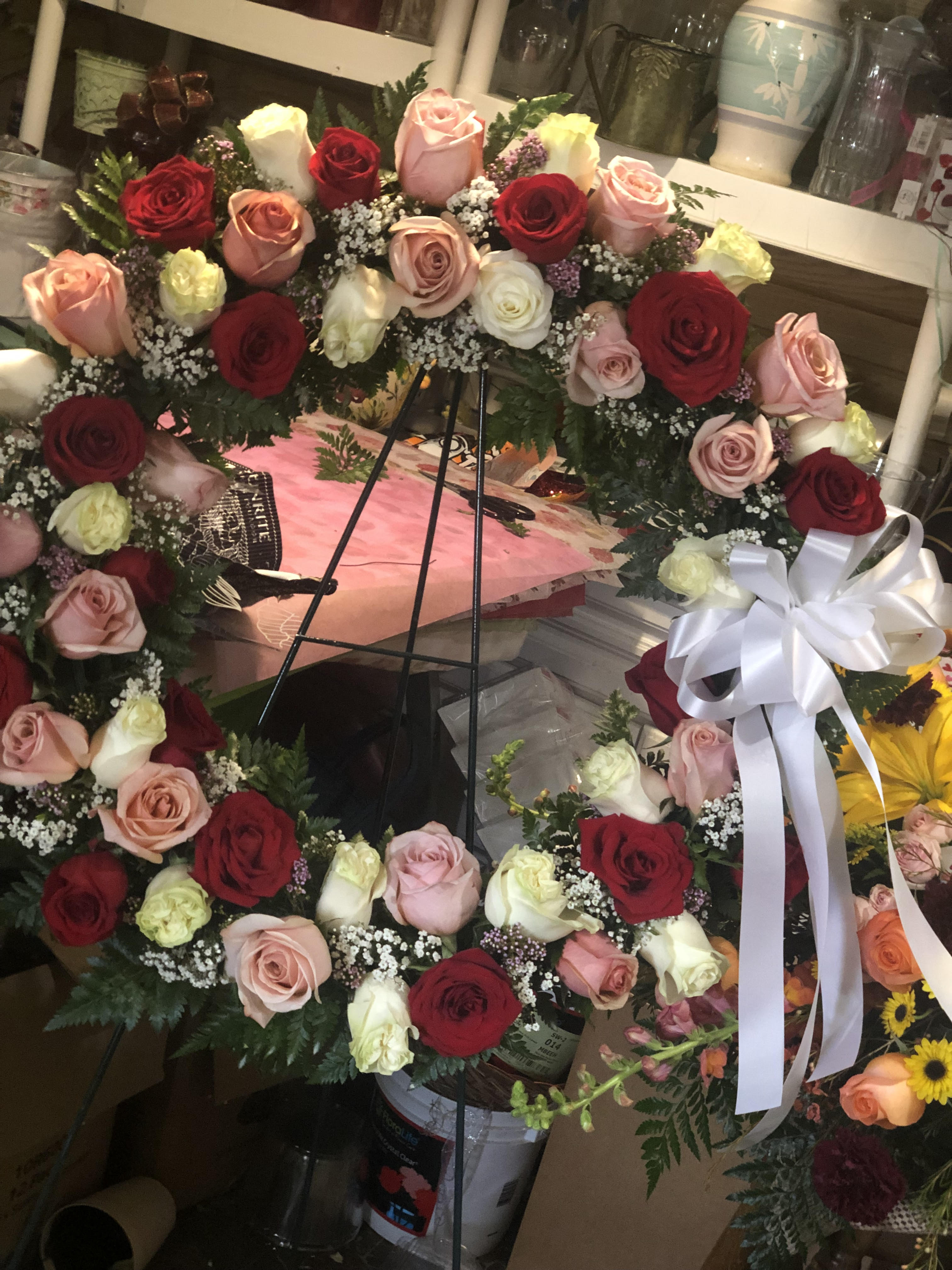 Large circular wreath of red, pink, and white roses with a white ribbon bow