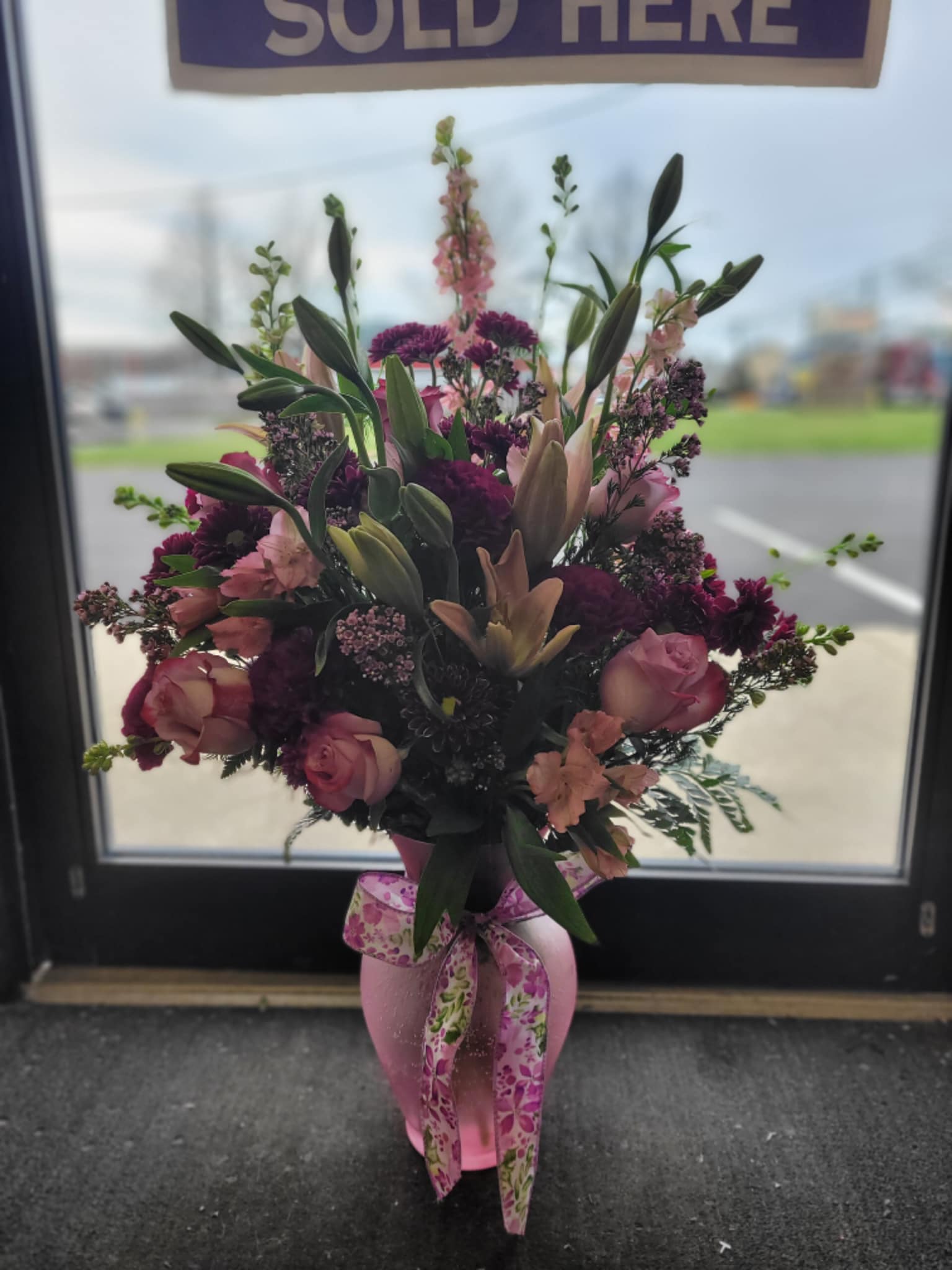 Pink and purple floral arrangement in a pink vase with a ribbon