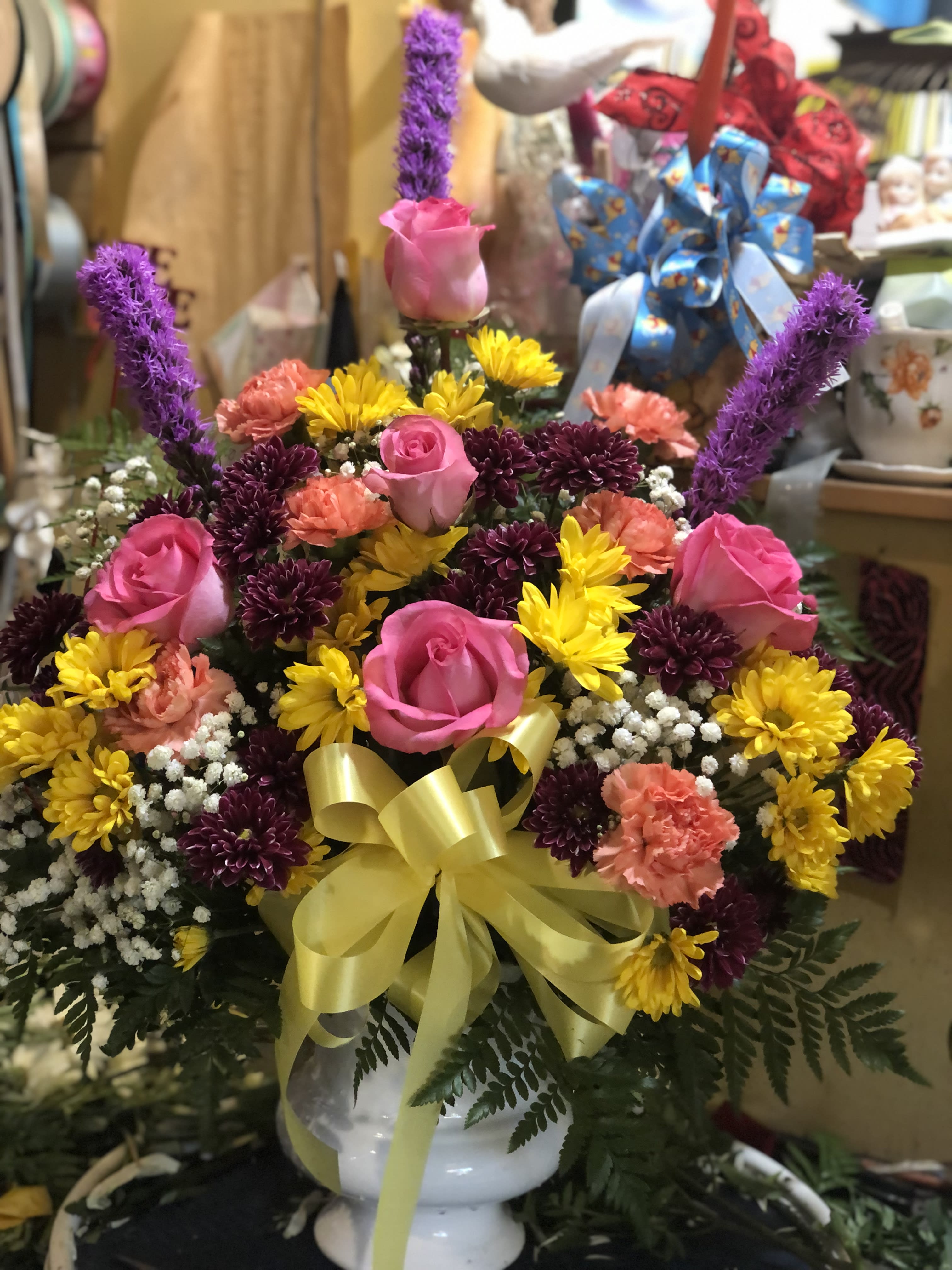 Pink roses and mixed daisies in a white vase with a yellow bow