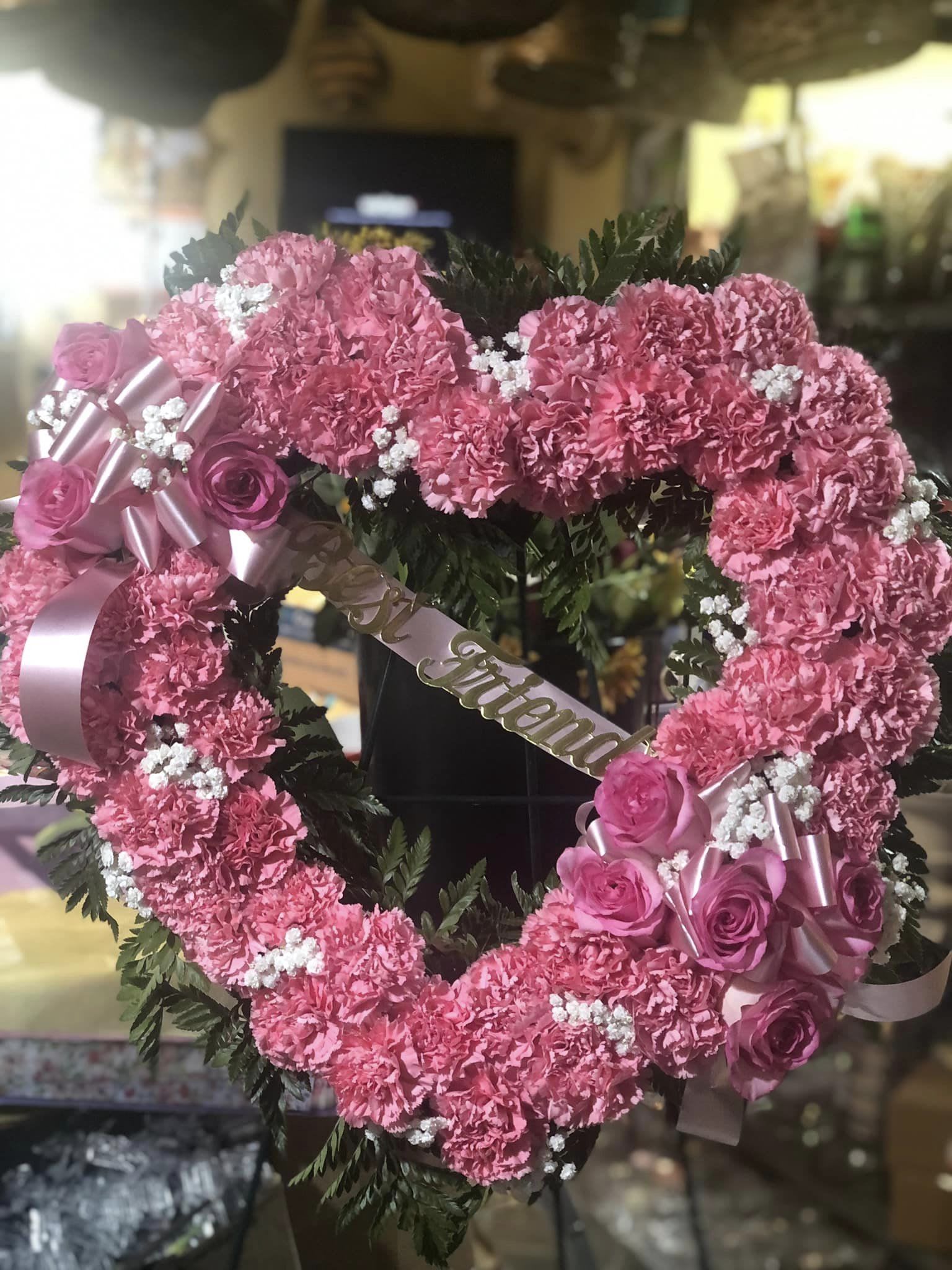 Pink floral heart wreath with roses and ribbon on a stand