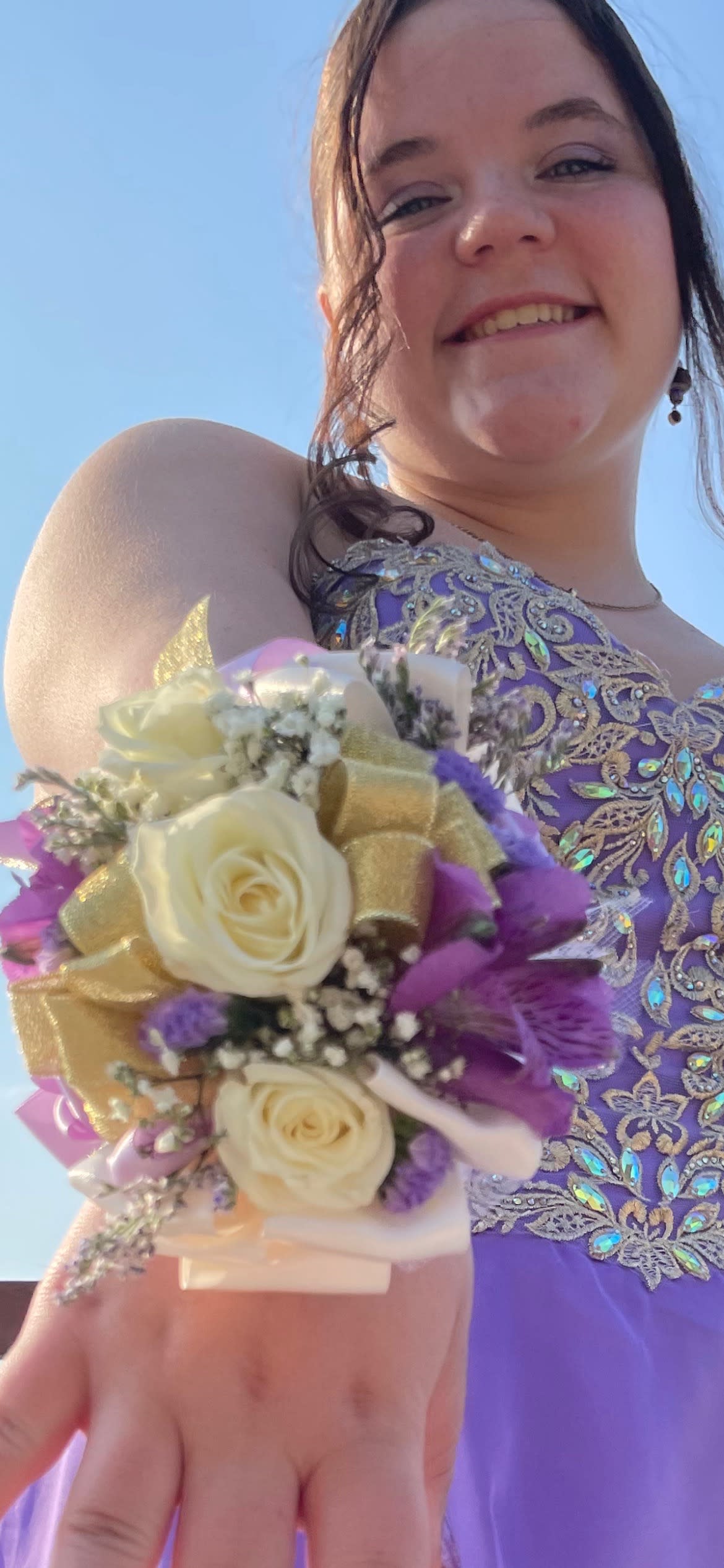 Girl wearing a purple dress holds a wrist corsage with cream roses and purple flowers