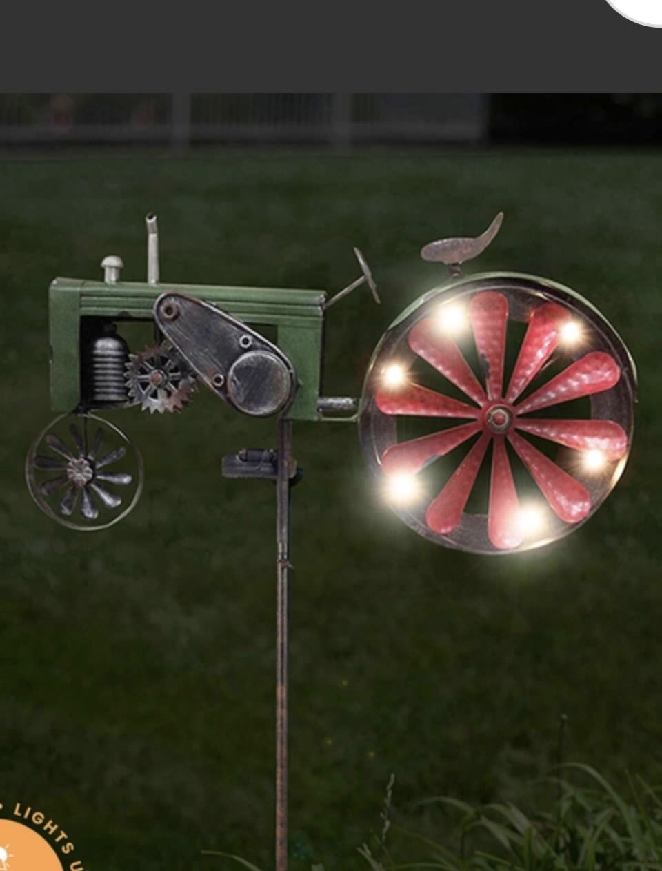 Tractor Garden Stake - Solar Spinner - This solar spinner does double duty by spinning in the breeze and lighting up with power from the sun! Standing over 5 feet tall, this kinetic spinner features red and green tractor, whose wheels light up with solar powered LED lights and spin in the breeze. This spinner makes a charming statement piece for any outdoor space and is designed to withstand the elements.  ??????? ???????: • Features rustic red and green tractor with LED lights on the back wheel • Crafted from color painted metal • Mounted on h-bottom stake • Easy assembly • Weather-resistant for year-round use  Height: 63" Width: 20.87"  Outdoor Decor | Weatherproof Yard Art | Whimsical Gifts | Garden Ornaments | Gifts for Gardeners | Seasonal Décor | Nature-Inspired Art