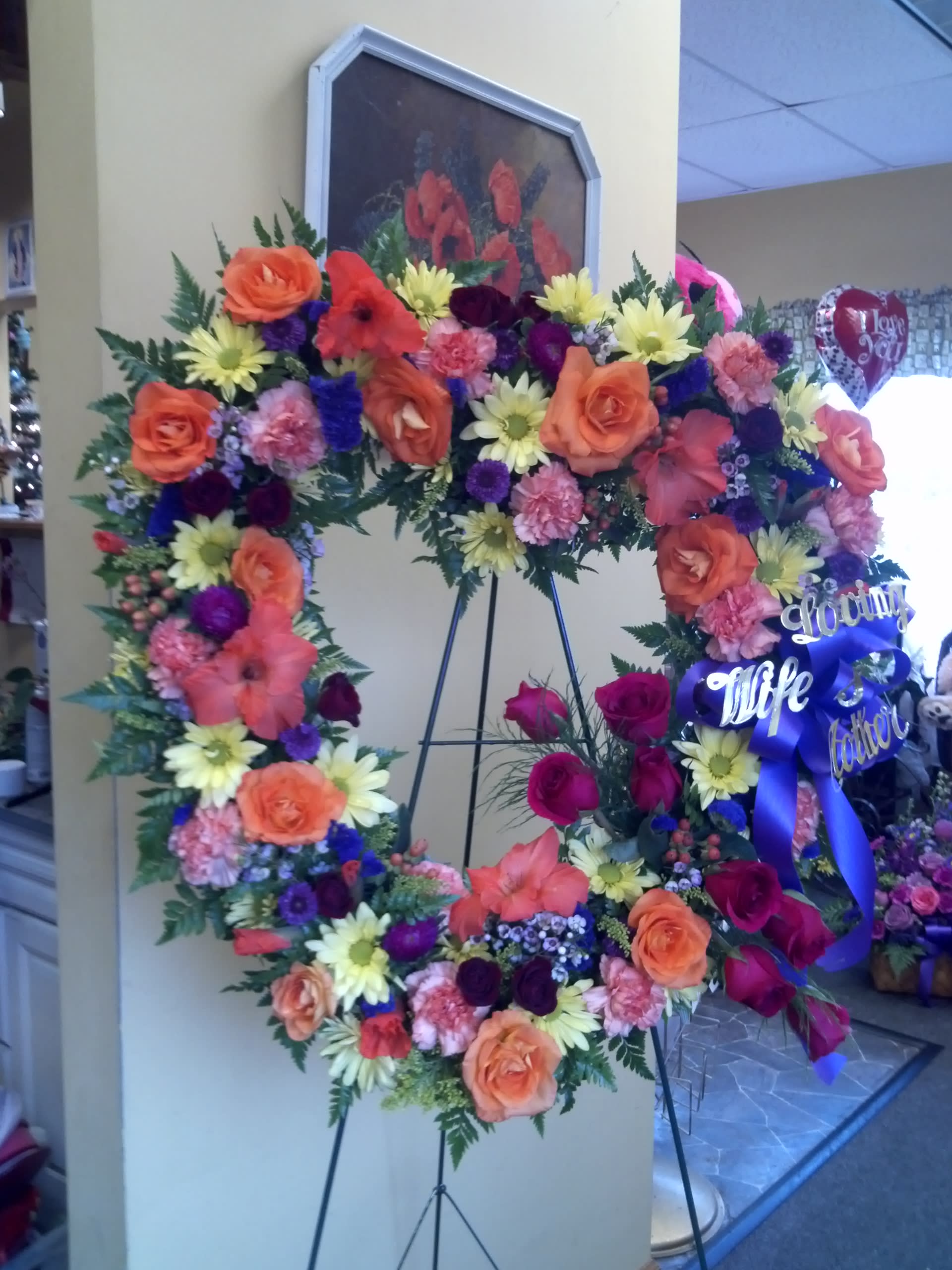 Large floral wreath on an easel with roses, daisies, and ribbon
