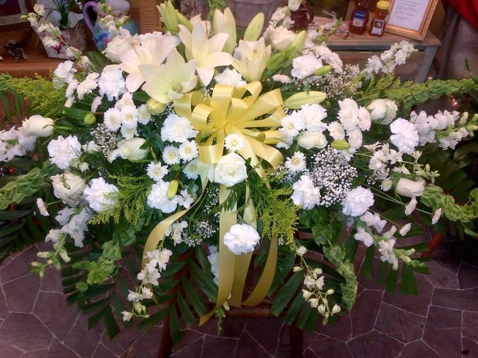 Large white floral spray with lilies, roses, and a yellow ribbon