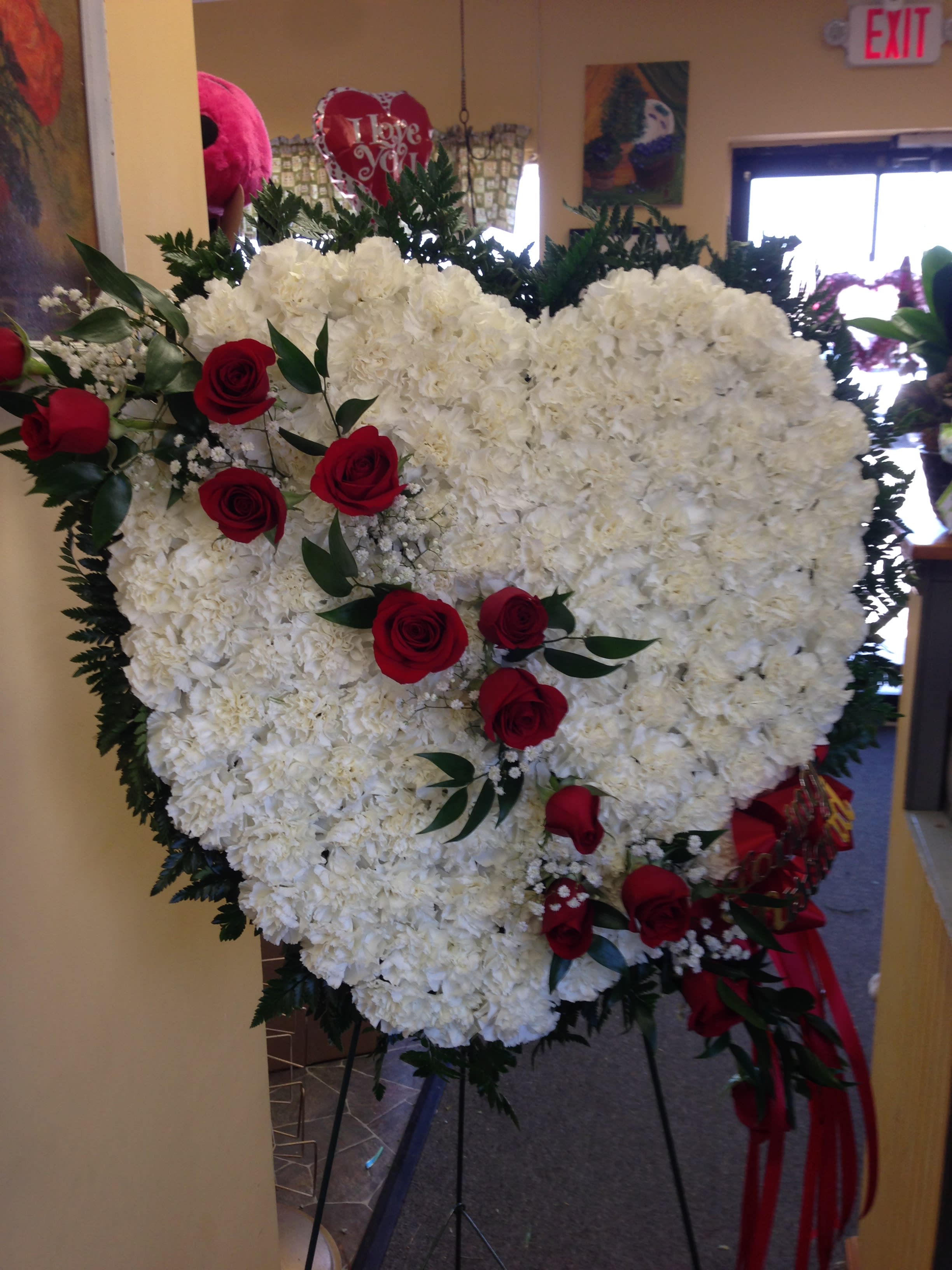 Heart-shaped white floral spray with red roses on a stand